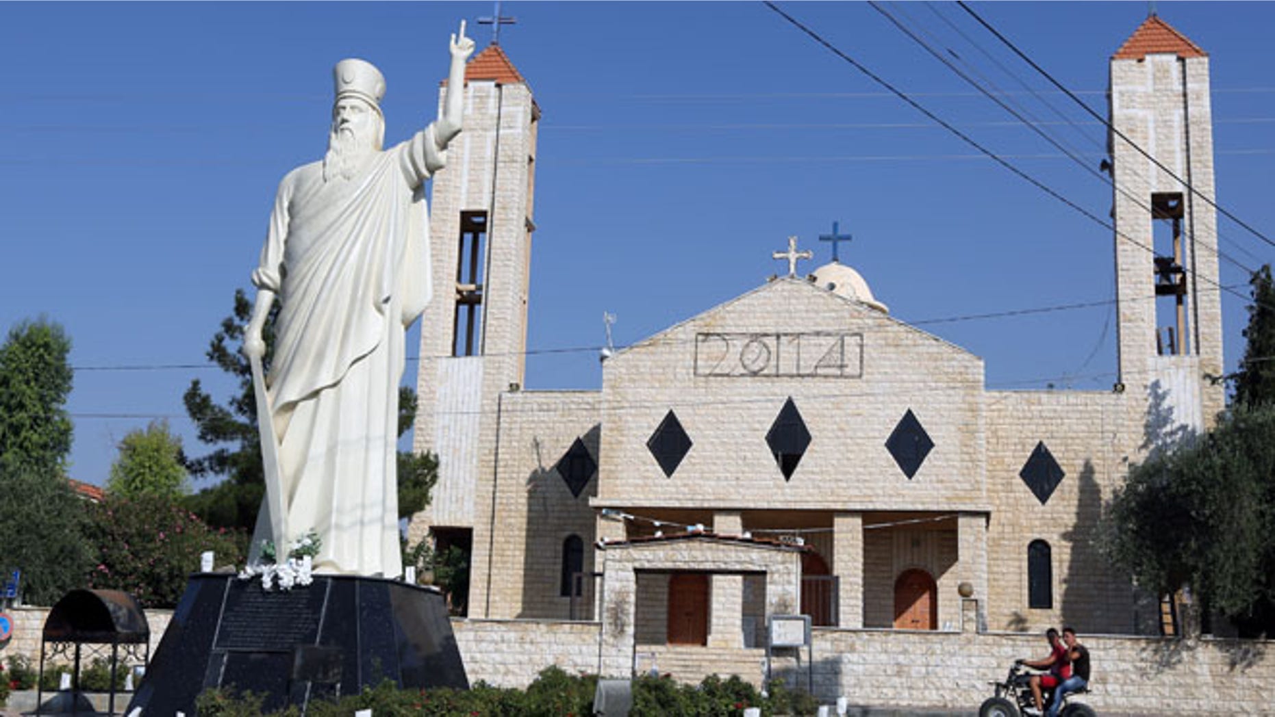 Aug. 13, 2014: Two young men ride a motorcycle past a church in Lebanon's Christian village of Ras Baalbek in the northern Bekaa region near the border with Syria. (AP)