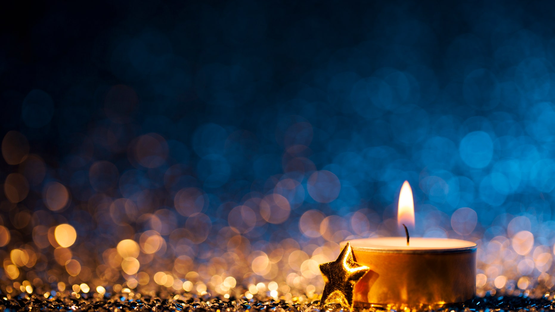 Tea light and a golden star on defocused blue and gold background.