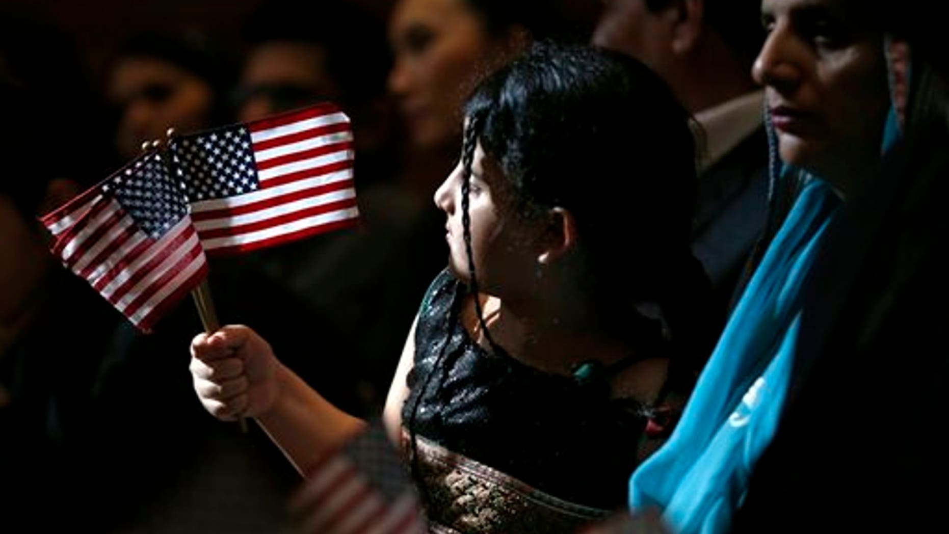 Sunlight peeking through a window at the Jersey City City Hall shines 5-year-old Anmol Sajid as she waves U.S. flags during a naturalization ceremony in which her mother, Uzma Gulzar, right, of Pakistan, was sworn in as United States citizen, Friday, April 25, 2014, in Jersey City, N.J. The U.S. Citizenship and Immigration Services claims the ceremony is the first- ever held at Jersey City City Hall. (AP Photo/Julio Cortez)