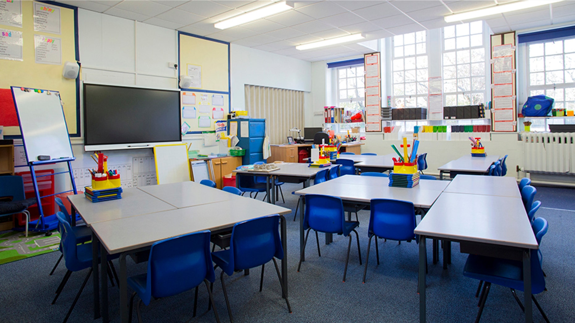 A horizontal image of an empty primary school classroom. The setting is typically British.