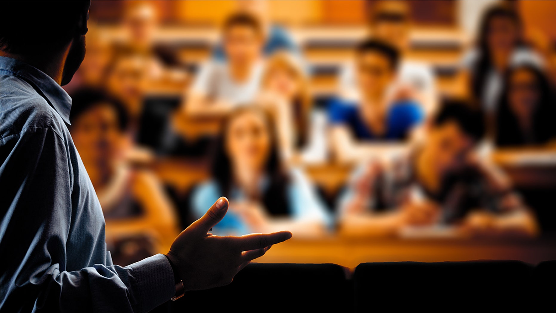 Large group of students sitting in the lecture hall at university and listening to their teacher. Focus on the professor. Dark tones.