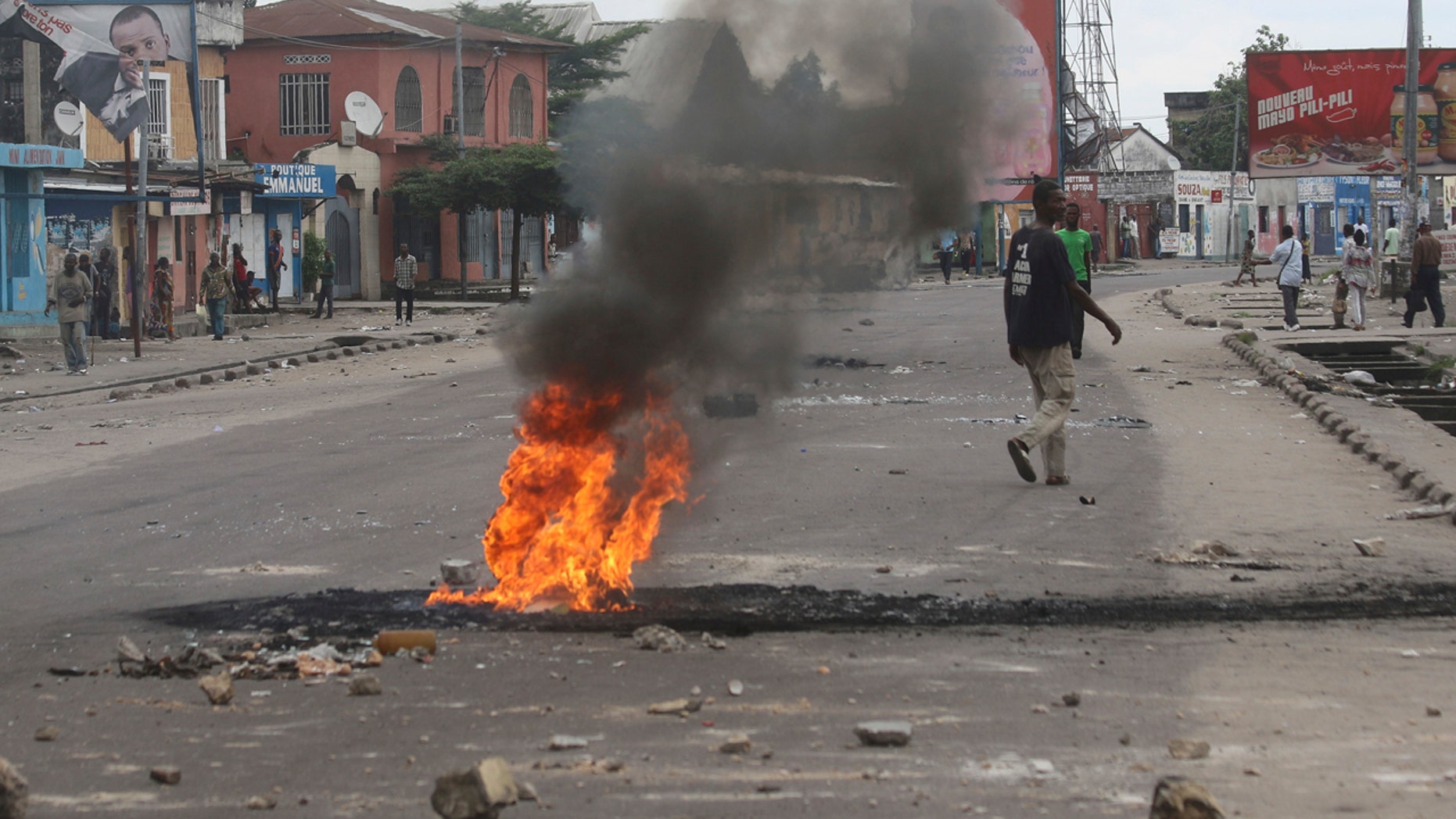 People walk near burning debris during protests in Kinshasa, Democratic Republic of Congo, Tuesday, Dec. 20, 2016.