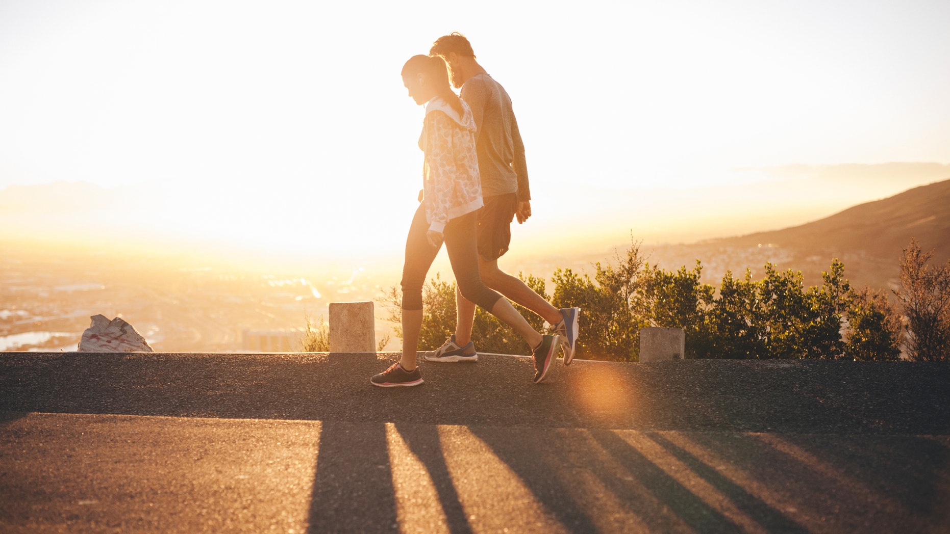 Couple walk along road at sunrise. Couple talking a walk on hillside road with bright sunlight.