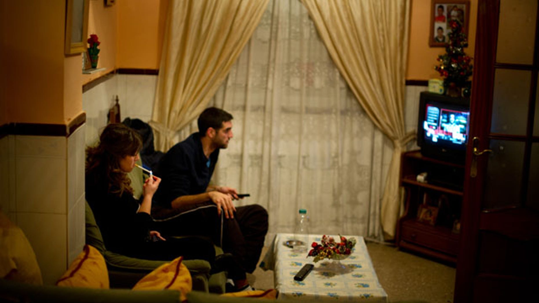 VILLACANAS, SPAIN - NOVEMBER 29: Unemployed twenty-year old Maria Regina Fernandez (L) spends the night watching television with her boyfriend, who does also not hold a job, instead of going out to the cinema or the villages bars and cafeterias, at their grandmothers home on November 29, 2012 in Villacanas, Spain. During the boom years, where in its peak Spain built some 800,000 houses a year accompanied by the manufacturing of millions of wooden doors, the people of Villacanas were part of Spain's middle class enjoying high wages and permanent jobs. During the construction boom years the majority of the doors used within these new developments were made in this small industrial town. Approximately seven million doors a year were once assembled here and the factory employed a workforce of almost 5700 people, but the town is now left almost desolate with the Villacanas industrial park now empty and redundant. With Spain in the grip of recession and the housing bubble burst, Villacanas is typical of many former buoyant industrial Spanish towns now struggling with huge unemployment problems. (Photo by Jasper Juinen/Getty Images)