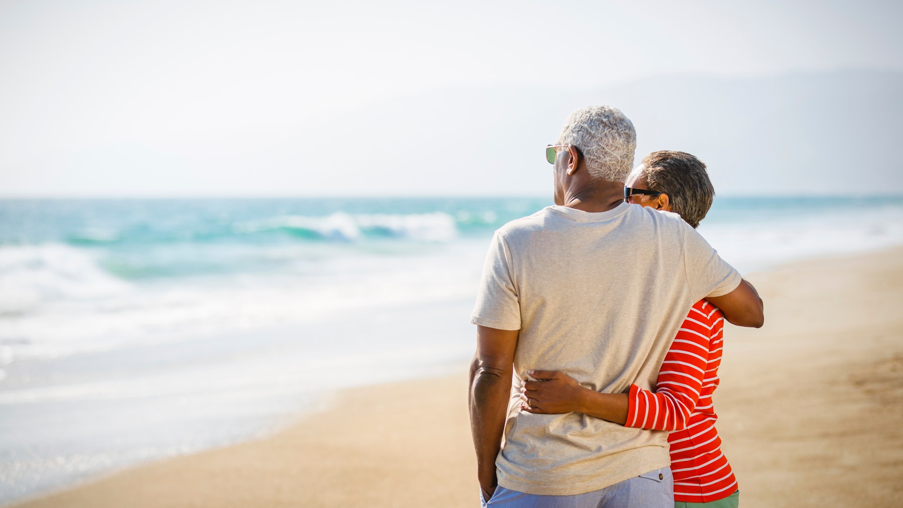 Senior African American couple embracing at sandy beach.