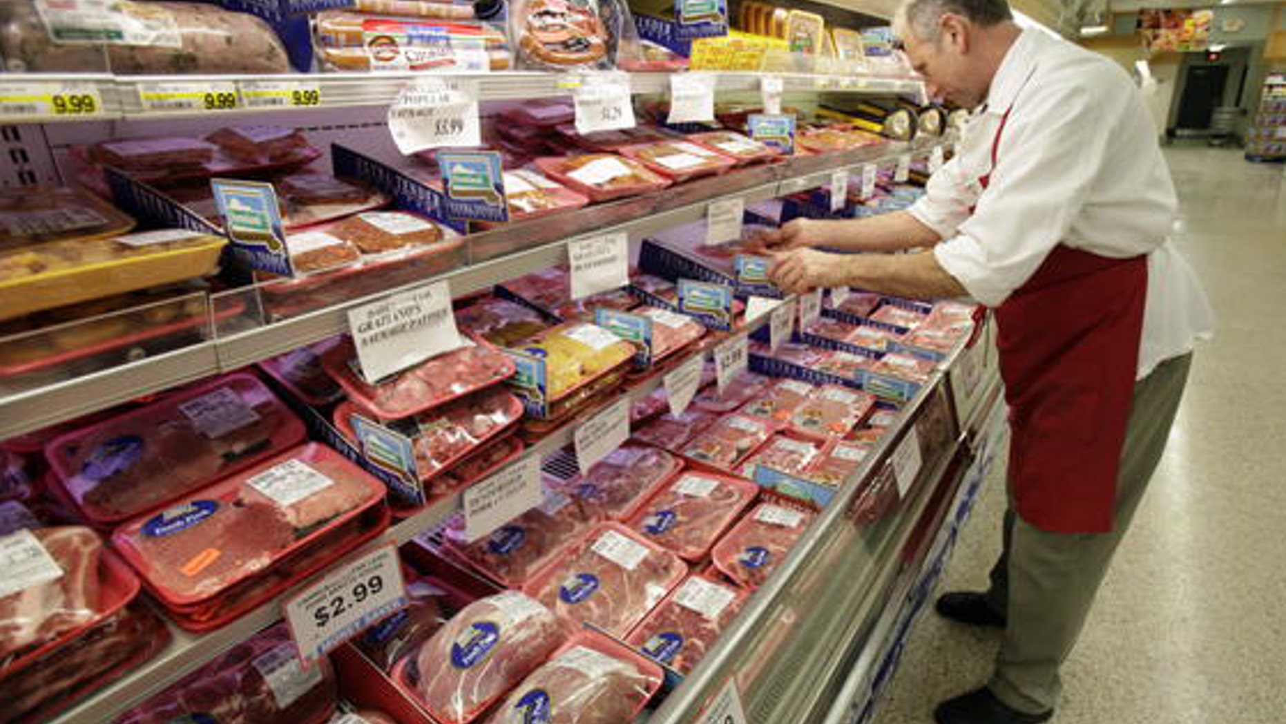A butcher looks at several cuts of meat at a grocery store.