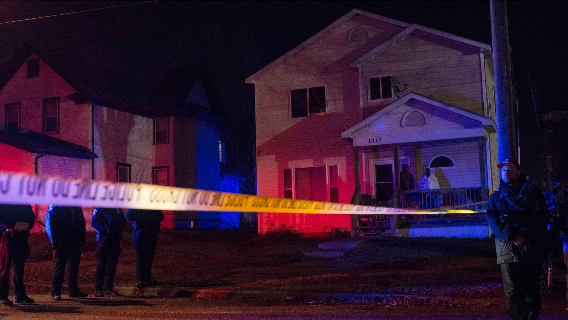 MINNEAPOLIS, MN - NOVEMBER 24: Police line up in front of a crime scene, and two people look on from their porch after 5 people were shot at a Black Lives Matters protest November 24, 2015 in Minneapolis, Minnesota. According to reports, a group of white men allegedly opened fire on the crowd after being escorted away from the encampment. (Photo by Stephen Maturen/Getty Images)