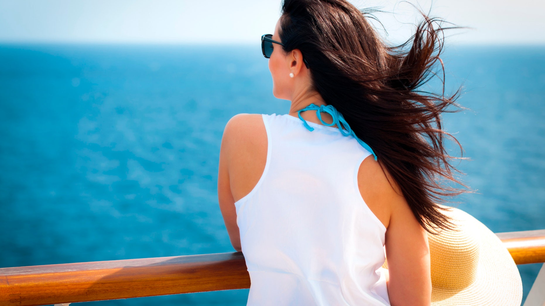 Woman wearing a floppy straw hat and a white dress standing next to the railing on a cruise ship