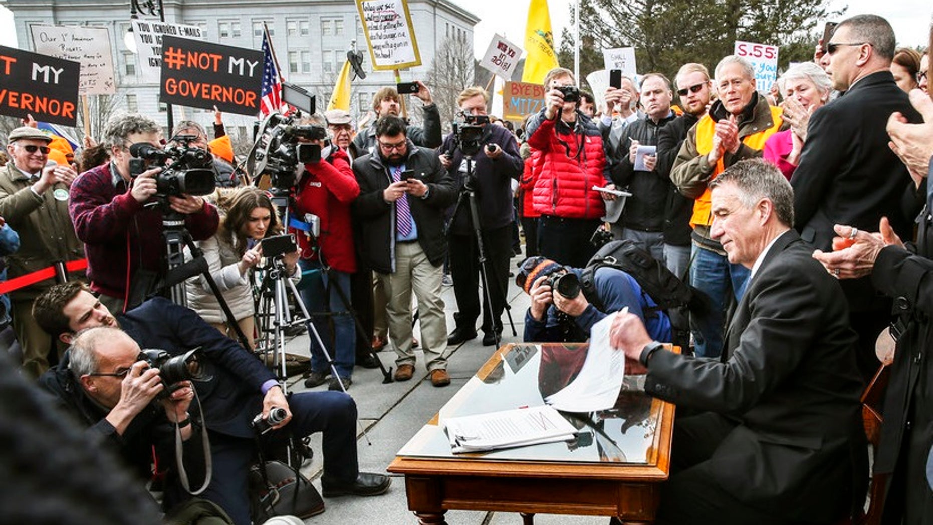 Facing signs that read "Not my governor" and amid taunts and jeers, Vermont GOP Gov. Phil Scott signed into law the state's first-ever sweeping gun control measures.