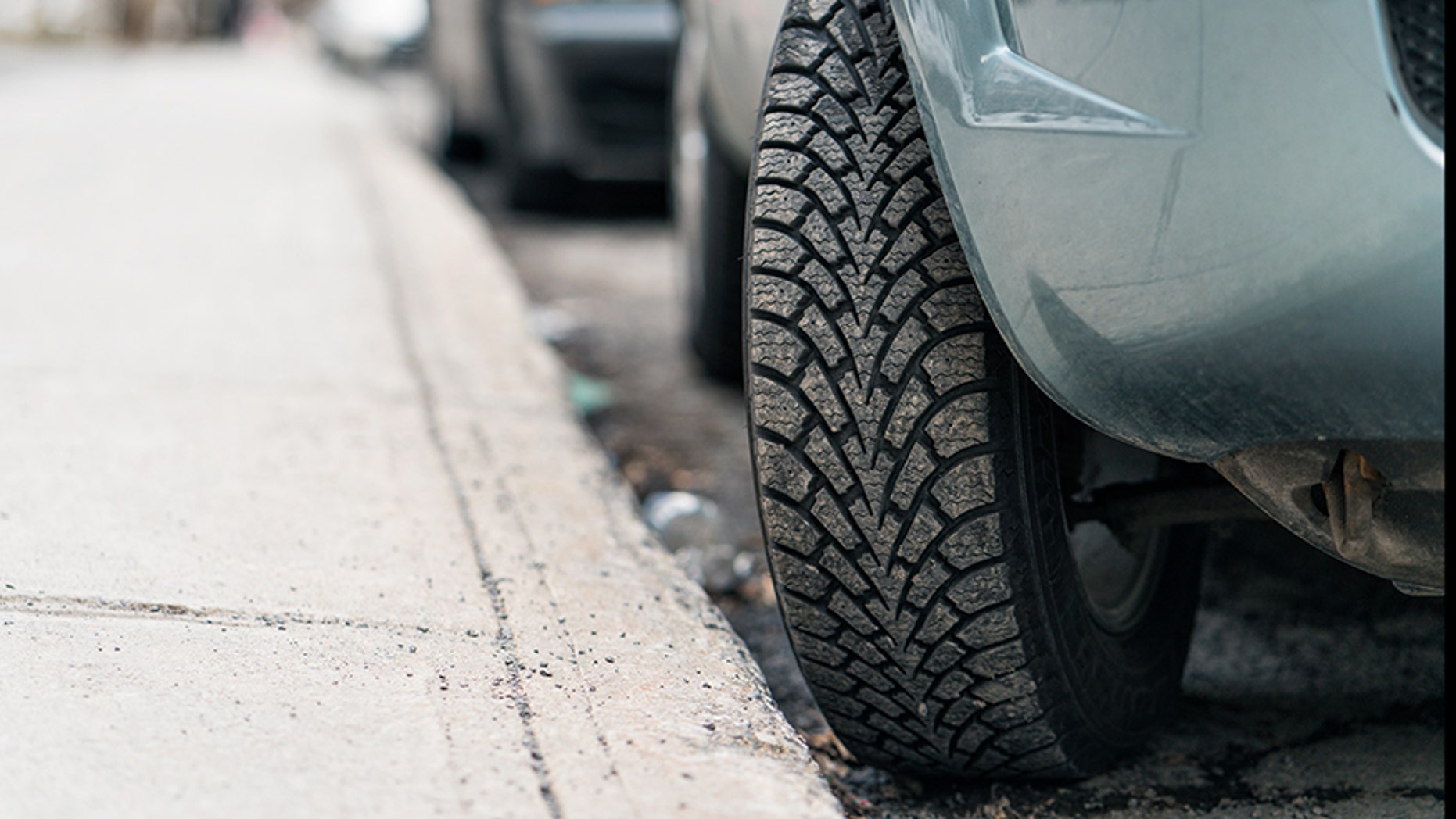 Close-up of a car parked on a hill, with the tire turned into the curb to stop the car from rolling forward.