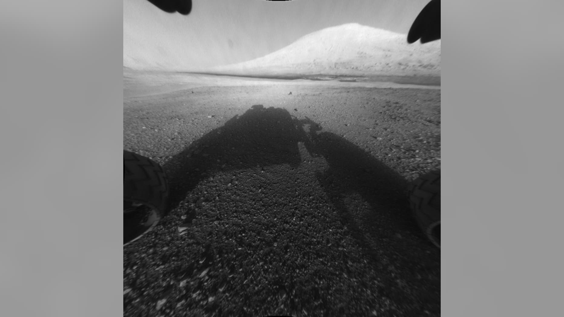 This image taken by NASA's Curiosity shows what lies ahead for the rover -- its main science target, Mount Sharp. The rover's shadow can be seen in the foreground, and the dark bands beyond are dunes.