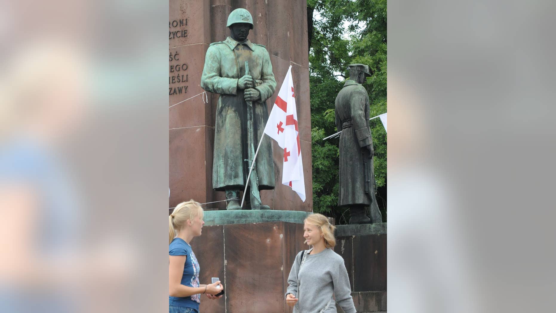 FILE - In this Aug. 13, 2008 file photo people walk past a 1945 monument of Polish-Soviet World War II brotherhood in arms, with Georgian national flags placed on it as a protest against Russia's involvement in Georgia, in Warsaw, Poland. Warsaw city councilors have banned the monument from being returned to its place in a city square, after it was temporarily removed from that square in 2011 to allow for the construction of a subway line in the area. (AP Photo/Alik Keplicz, File)