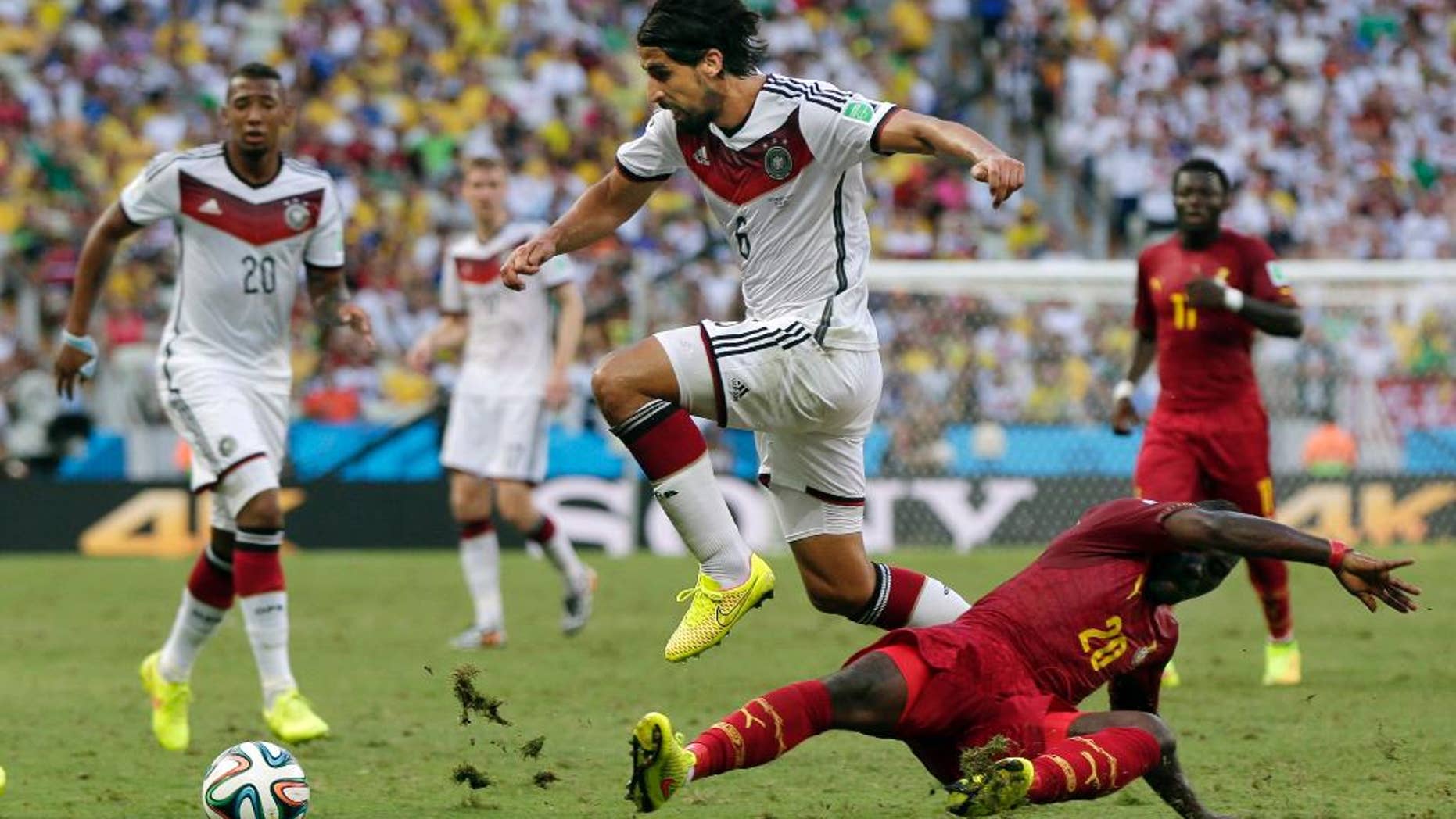Germany's Sami Khedira, center, jumps over Ghana's Kwadwo Asamoah, right, to attack with the ball during the group G World Cup soccer match between Germany and Ghana at the Arena Castelao in Fortaleza, Brazil, Saturday, June 21, 2014. (AP Photo/Marcio Jose Sanchez)