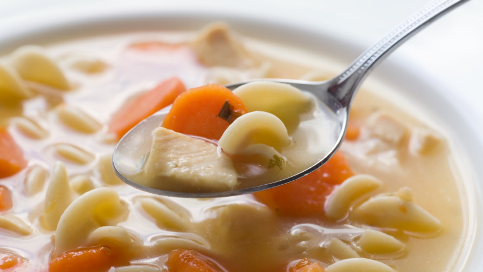 A bowl of chicken noodle soup. Focus is on the front of the spoon.