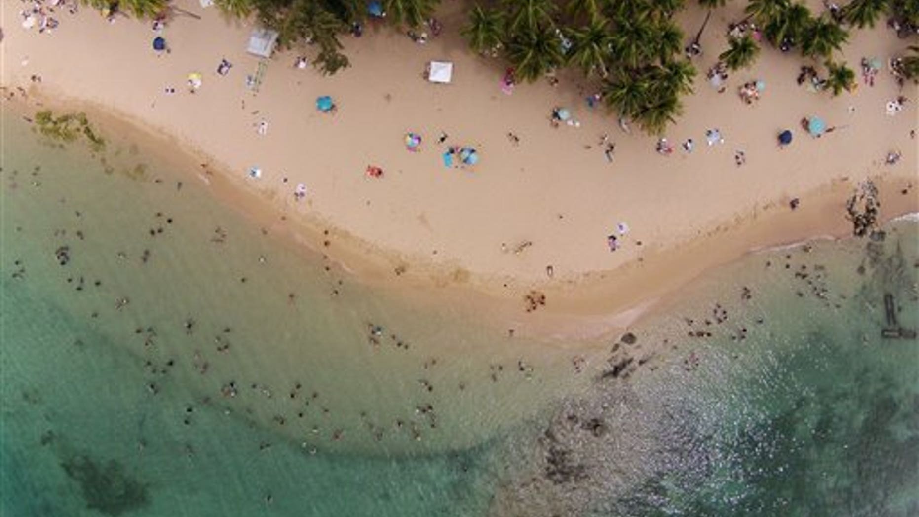 This July 16, 2014, photo, shows an aerial view of people enjoying the beach in San Juan, Puerto Rico. The territory's government has managed its first balanced budget in more than a decade. Sales tax revenues are up and its publicly owned power company has won breathing room to pay its debts. (AP Photo/Ricardo Arduengo)
