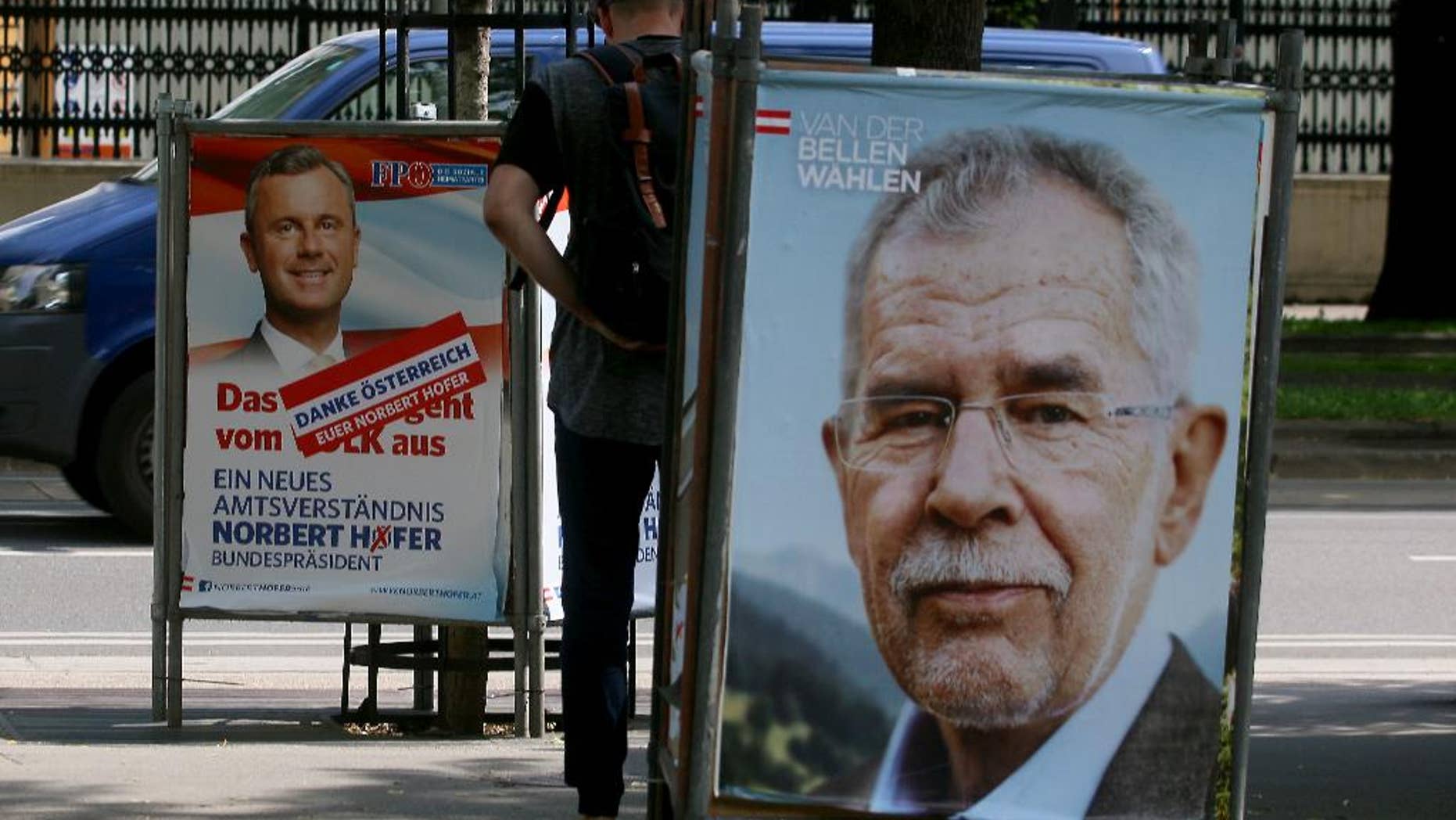 A man walks between election posters of Alexander Van der Bellen, candidate for presidential elections and former head of the Austrian Greens, right, and Norbert Hofer, candidate for presidential elections of Austria's right-wing Freedom Party, FPOE, left, in Vienna, Austria, Monday, May 23, 2016. The Eurosceptic, anti-immigration right-winger Norbert Hofer, and his left-leaning rival are neck and neck in Austria's presidential election a day after polls closed, and officials are now counting absentee ballots to determine who will win. (AP Photo/Ronald Zak)