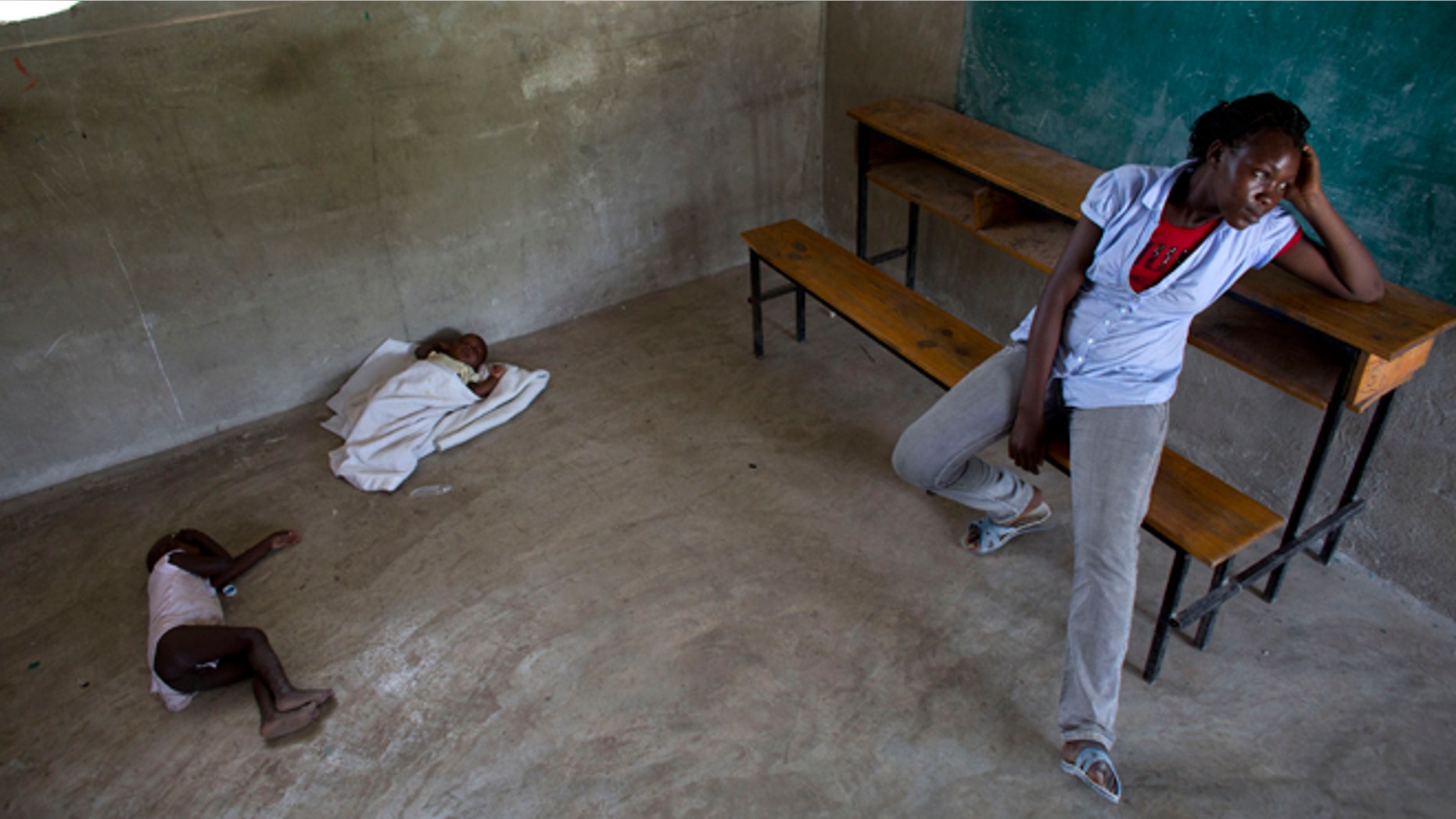 Milene Monime, 16, sits as her two-month-old son Jefferson Thezon, center, sleeps next to another person's child inside a school classroom where her family and others are staying after being deported the previous day from neighboring Dominican Republic, in the village of Fonbaya, Haiti, Thursday, June 18, 2015. People began preparing Thursday for deportation from the Dominican Republic after failing to obtain legal residency as part of a government program to crack down on migrants, most of them from neighboring Haiti or of Haitian descent. (AP Photo/Rebecca Blackwell)