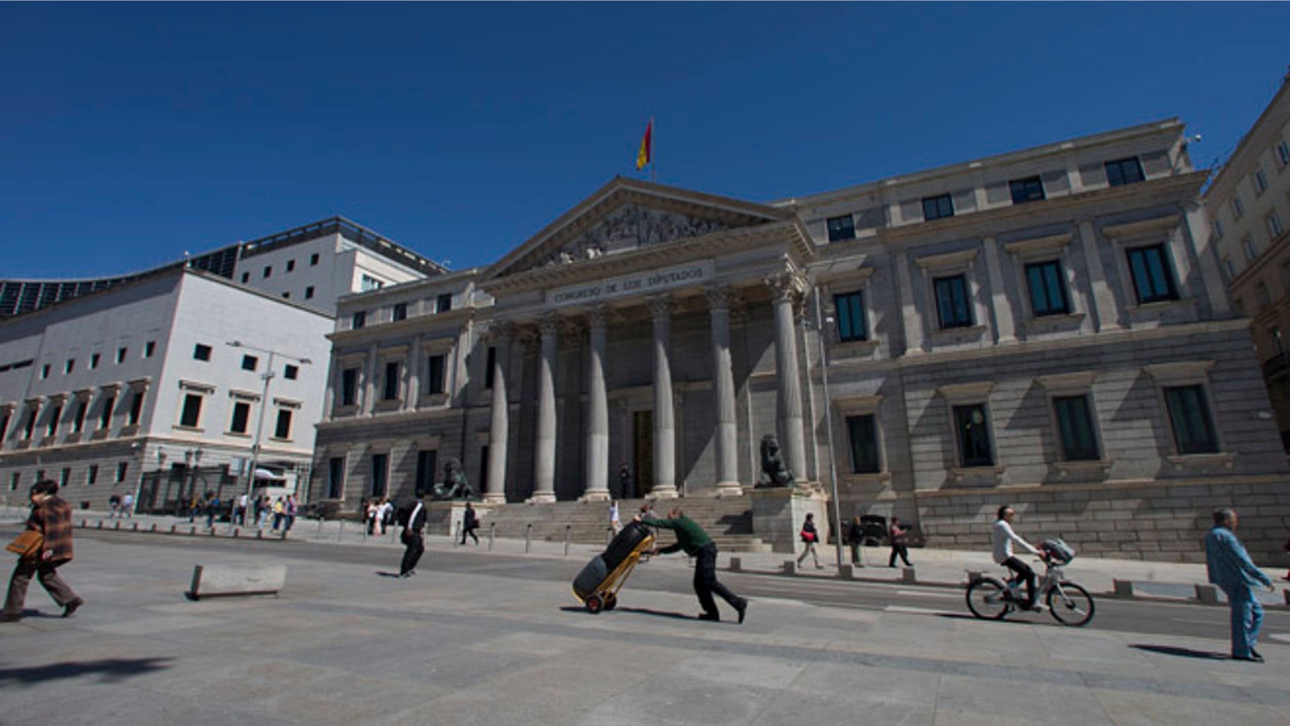 In this Tuesday, May 3, 2016 file photo, a worker pushes a trolley past the Spanish Parliament in Madrid, Spain, Tuesday, May 3, 2016. Spain is about to pass 300 days without a government. But guess what? Few people seem very bothered by that as the economy roars ahead. In Spanish cities there are packed terrace cafes and restaurants, thriving fashion shops and art galleries. The overall impression is of a bustling and vibrant country pressing forward. (AP Photo/Paul White, File)