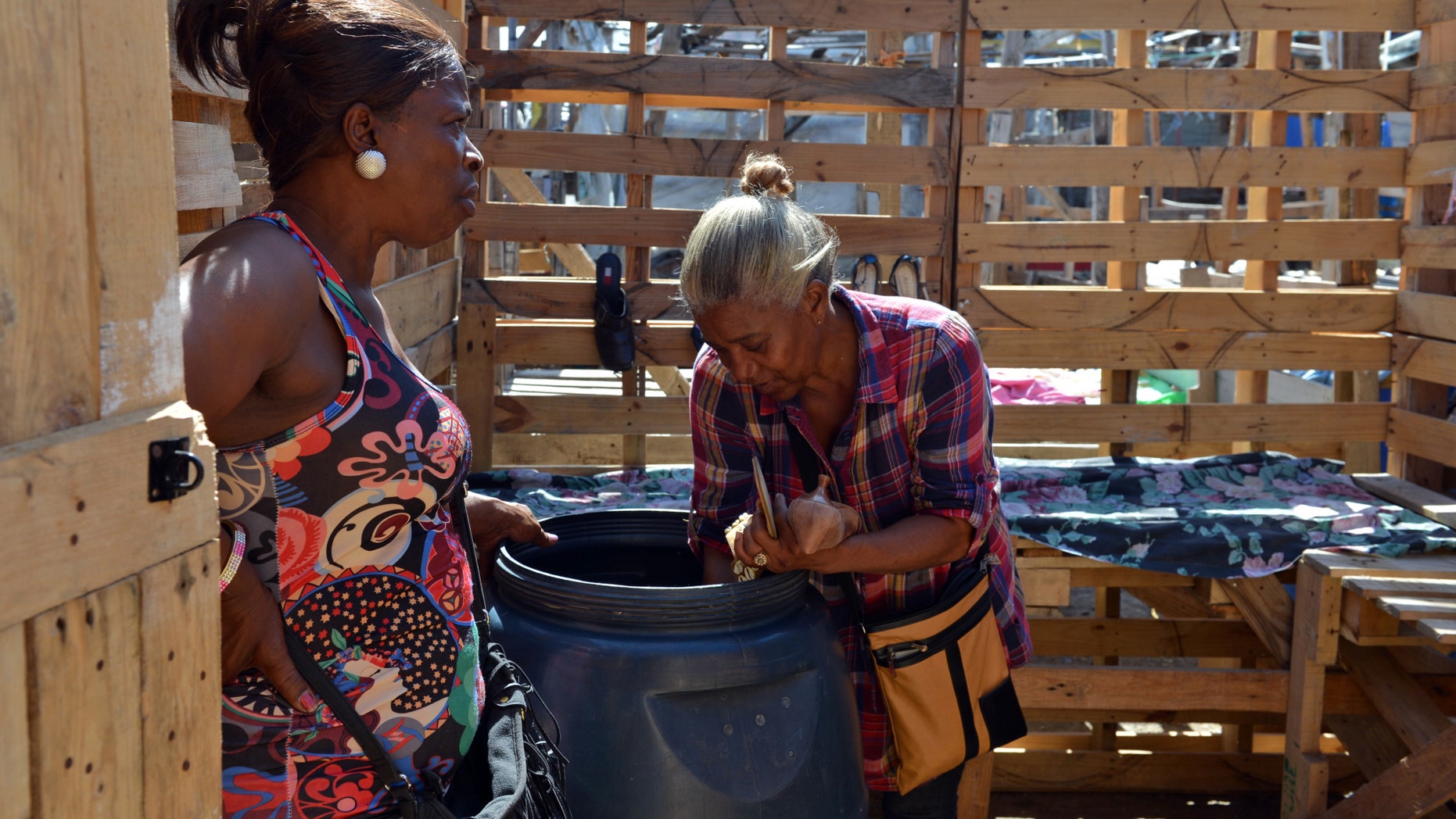 In this April 13, 2013 photo, Claudette Johnson, right, is accompanied by a friend while unpacking used clothing to sell at her stall at an outdoor market in West Kingston, Jamaica. Johnson still has a hard time sleeping at night a decade after her son was fatally shot in a confrontation with Jamaican police and 15 years after her taxi driver husband was murdered by gunmen. Year after year, both cases have collected dust in the island's gridlocked court system, leaving her in limbo. (AP Photo/David McFadden)