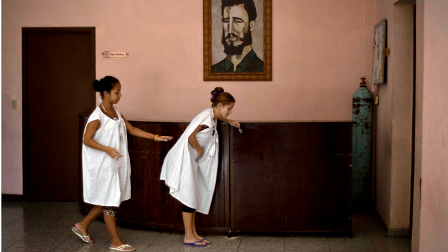 In this Oct. 27, 2014 photo, a pregnant woman is helped by another as she suffers from labor pains, while walking in front of a painting of Fidel Castro at a special maternity unit for high-risk pregnancies in Havana, Cuba. The island nation is in the midst of a broad campaign to drive up a birth rate that has fallen to the lowest in Latin America after years of fewer births, that mean that the number of working-age people in Cuba is expected to shrink starting next year, terrible news for an island attempting to jumpstart its stagnant centrally planned economy. (AP Photo/Ramon Espinosa)
