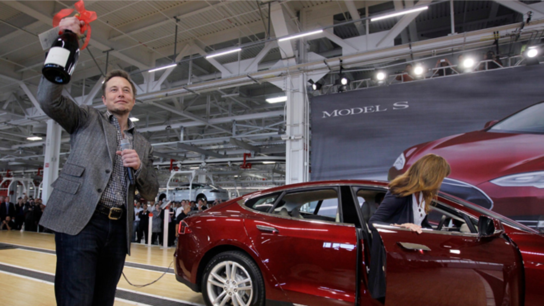 FILE - In this June 22, 2012 file photo, Tesla Motors Inc. CEO Elon Musk holds up a bottle of wine given as a gift from one of their first customers, right, during a rally at the Tesla factory in Fremont, Calif. Tesla Motors says it is preparing a site near Reno, Nevada, as a possible location for its new battery factory, but is still evaluating other locations. (AP Photo/Paul Sakuma, File)
