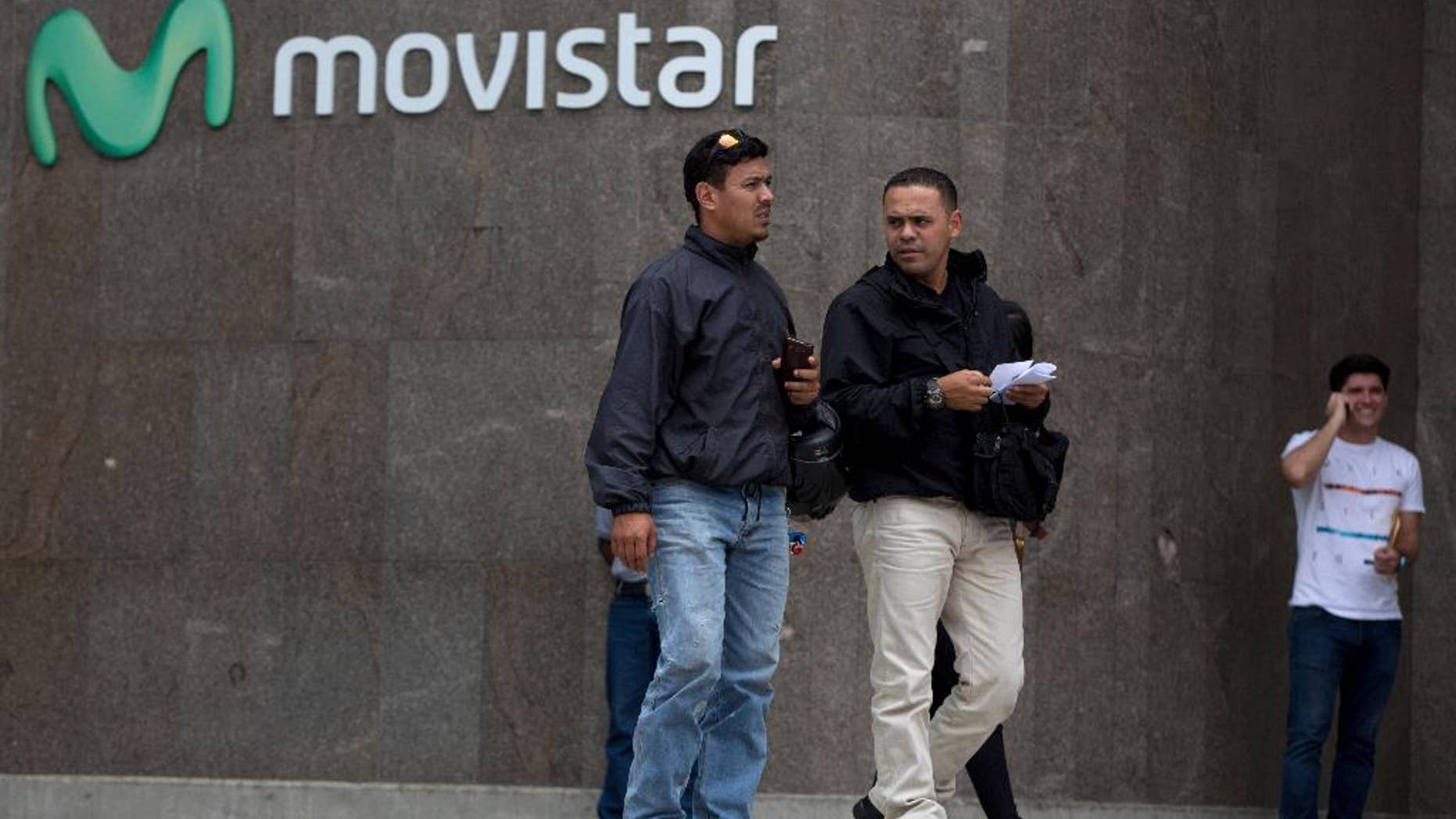Pedestrians walk outside Movistar a cell phone company office in the Chacao municipality of Caracas, Venezuela, Monday, April 11, 2016. Movistar, a subsidiary of the Spanish-based Telefonica, and Digitel both announced last week that they would be cutting international service because of issues related to Venezuela's byzantine currency controls. (AP Photo/Fernando Llano)