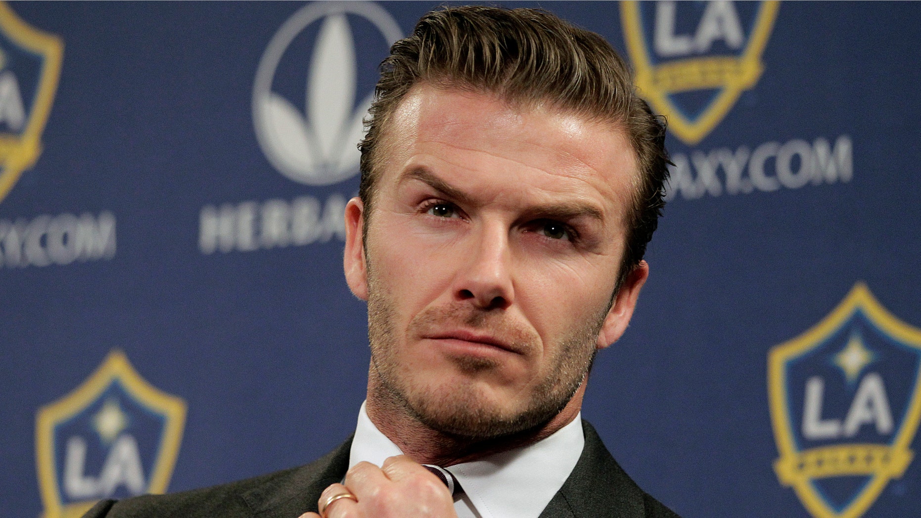 FILE - In this Jan. 19, 2012 file photo, Los Angeles Galaxy's David Beckham fixes his tie during a news conference in Los Angeles. Beckham says he is retiring from soccer at the end of the season. The 38-year-old Beckham recently won a league title in a fourth country with Paris Saint-Germain. He has become a global superstar since starting his career at Manchester United. (AP Photo/Jae C. Hong, File)