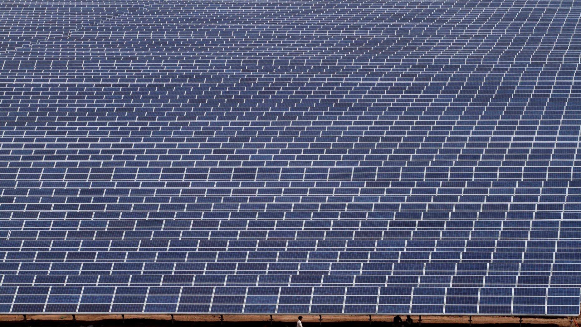 Indian workers walk past solar panels at the Gujarat Solar Park at Charanka in Patan district, about 250 kilometers (155 miles) from Ahmadabad, India, Saturday, April 14, 2012. Gujarat state Chief Minister Narendra Modi will dedicate the 200 megawatt solar power park, along with other solar projects totaling 600 megawatts of power on April 19. (AP Photo/Ajit Solanki)
