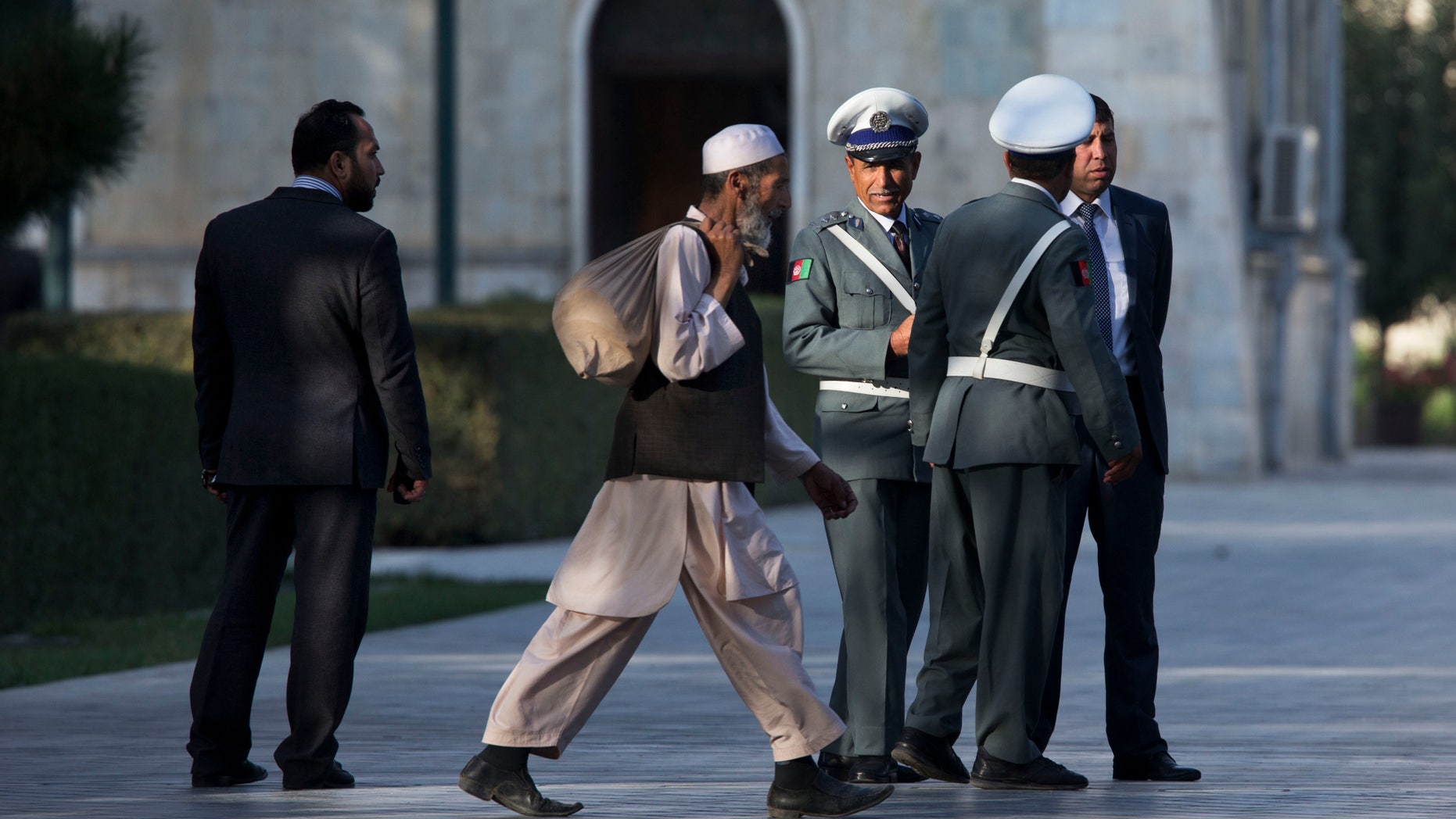 A worker walks past Afghan guards as they wait for a news conference that has been delayed between U.S. Secretary of State John Kerry and Afghan President Hamid Karzai at the presidential palace on the second day of an unannounced stop in Kabul, Afghanistan, on Saturday, Oct. 12, 2013. Kerry extended talks Saturday with Karzai on a bilateral security agreement with the United States, and while work remains to be done a deal could be struck by the end of the day, a presidential spokesman said. (AP Photo/Jacquelyn Martin, Pool)