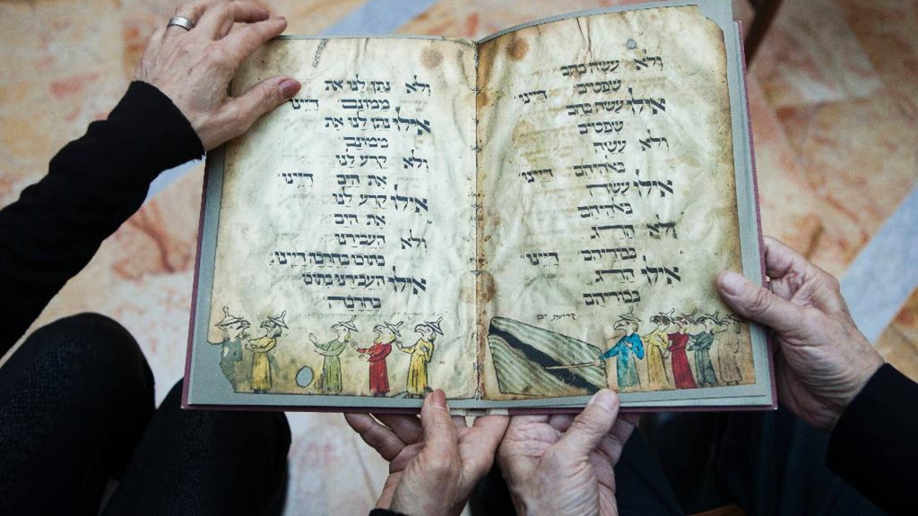 File - In this file photo taken Wednesday, April 13, 2016, Eli and Shuli Barzilai hold a copy of the Birds' Head Haggadah, the text read around Jewish dinner tables on the Passover holiday, in their home in Jerusalem. Last year, the descendants of German Jewish lawmaker Ludwig Marum requested the Israel Museum pay compensation for the famed Bird's Head Haggadah. They say the Haggadah was snatched from their grandfather's family after he was rounded up by the Nazis and later sold to the predecessor of the Israel Museum in Jerusalem without their consent. (AP Photo/Dan Balilty, File)