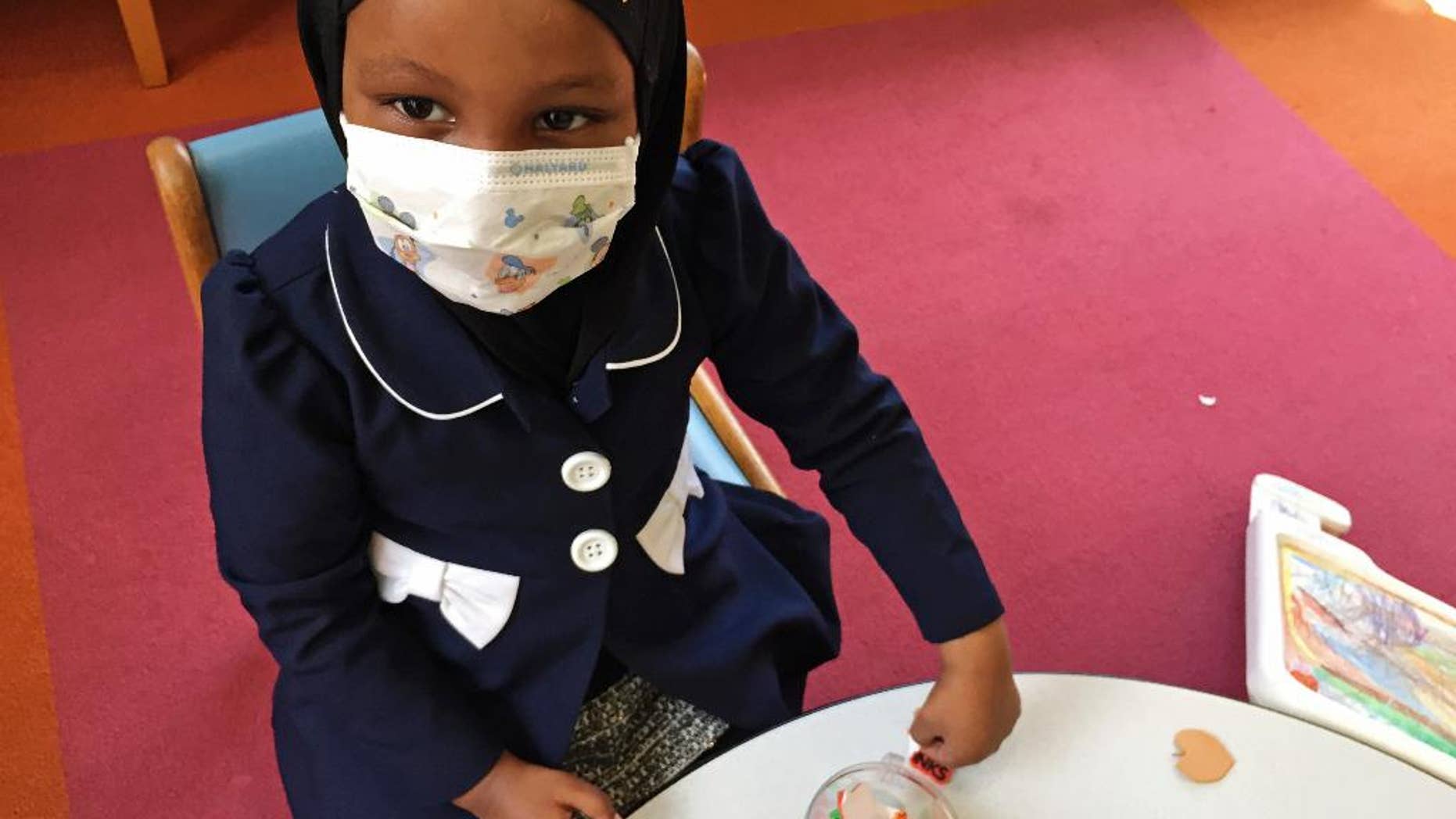 In this Tuesday, May 2, 2017 photo, Amira Hassan, of Burnsville, Minn., plays in the waiting room at the specialty clinic at Children's Minnesota in Minneapolis. Hassan went to the hospital's clinic for a routine wellness check, but had to wear a mask to protect her from measles after an outbreak has sickened more than 30 children in Minnesota. The masks are just one precaution that hospitals are taking to try to control the spread of the disease, which is predominantly affecting Minnesota's Somali community. (AP Photo/Amy Forliti)