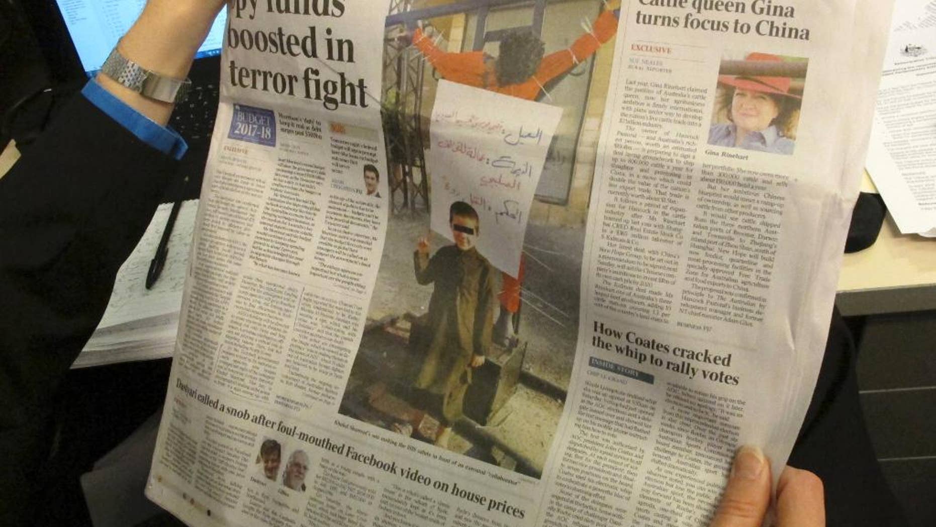 This photo published on the front page of the Monday, May 9, 2017, edition of "The Australian" newspaper shows says a 6-year-old Australian boy making an Islamic State movement salute in front of a human body hanging from a cross somewhere in the Middle East, in Canberra. Australian Prime Minister Malcolm Turnbull said on Monday such children who returned from the battle fields of Syria and Iraq would be subjected to "the closest attention" to ensure Australian are safe. (AP Photo/Rod McGuirk)