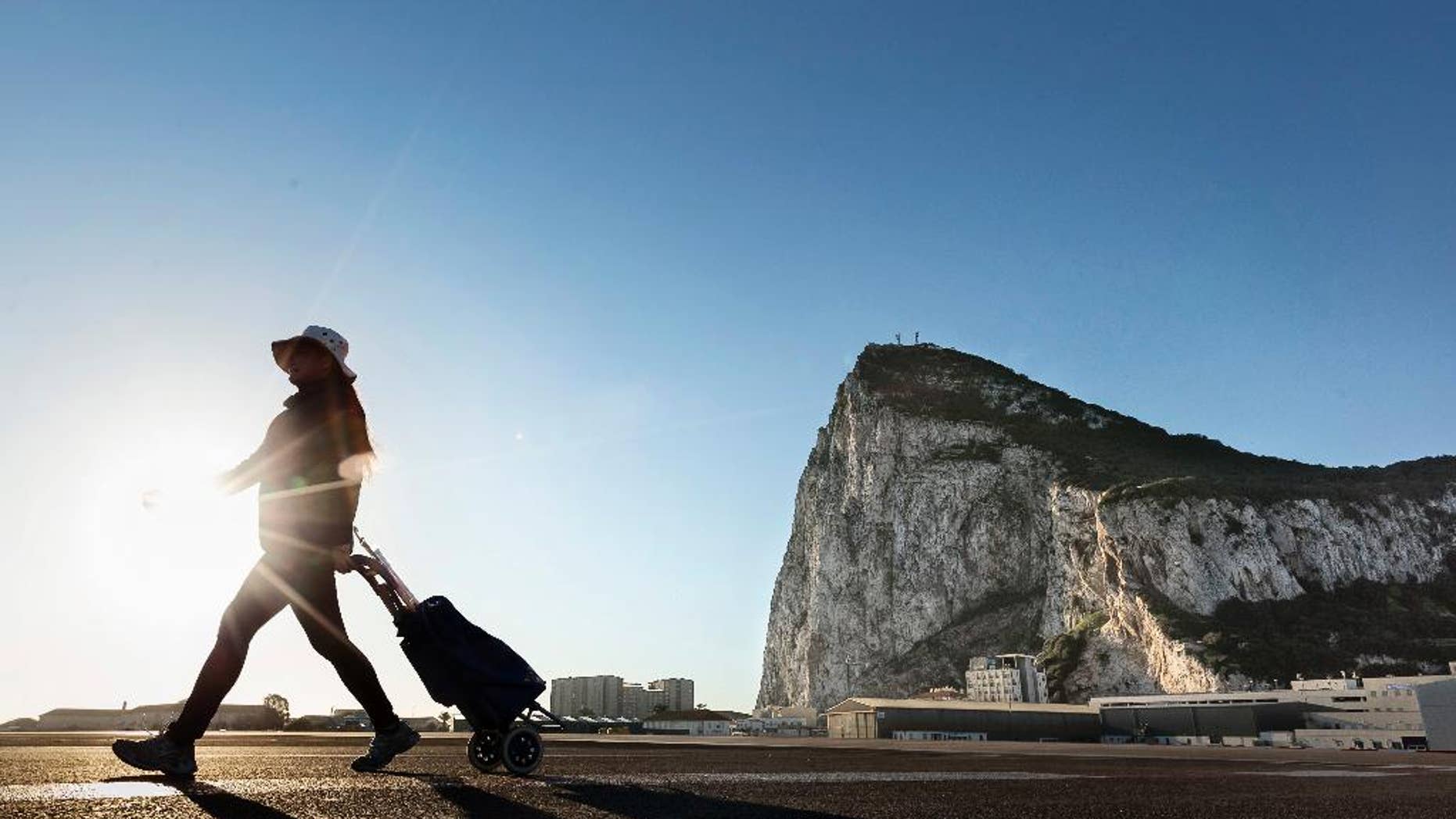 FILE- In this Wednesday, March 1, 2017 file photo, a woman walks on the Spanish side of the border between Spain and the British overseas territory of Gibraltar with the Rock of Gibraltar in the background, in La Linea de la Concepcion, Spain. Deep inside the Rock of Gibraltar is a room known as The Vault. Dug by the British army in World War Two, the room now houses servers that power the websites of dozens of international online gambling companies. Those companies were lured to this speck of British territory on Spain's southern tip by its low taxes and its unimpeded access to the European Union's single market of around 500 million people. Britain's looming departure from the EU, therefore, has cast a cloud over Gibraltar's future because Brexit could see it shut off from the rest of the EU.(AP Photo/Daniel Ochoa de Olza, File)