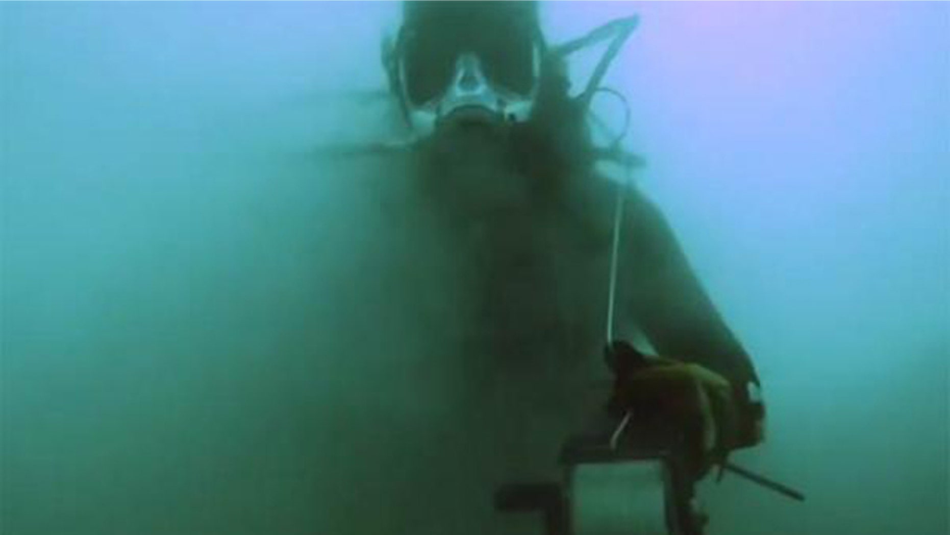 A diver, outfitted with special equipment designed to brave the salty conditions, is partially obscured by the murk of the Dead Sea.