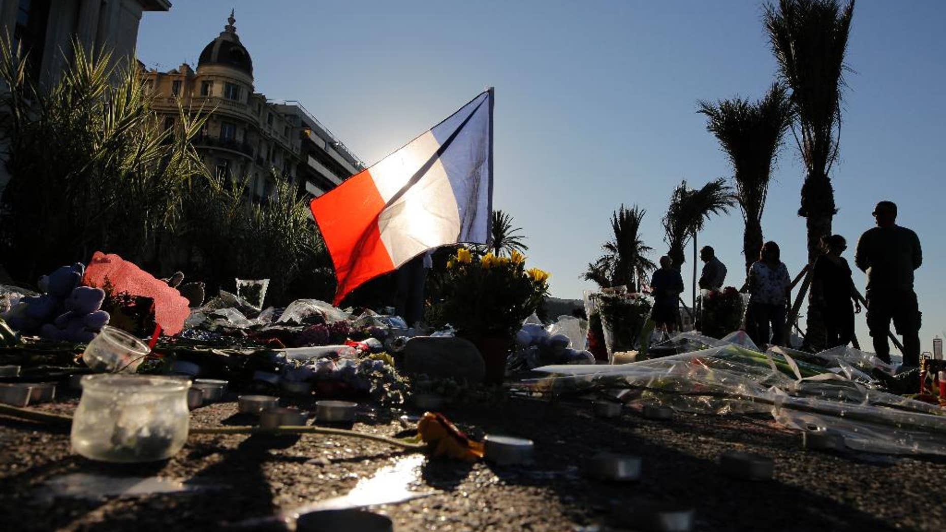 FILE - In this Sunday, July 17, 2016 file photo, a French flag stands among a floral tribute for the victims killed during a deadly attack, on the famed Boulevard des Anglais in Nice, southern France. Residents of the French Riviera city of Nice that lived through the truck rampage horror in July 2016, are reliving it this week following a chillingly similar narrative in Berlin. (AP Photo/Laurent Cipriani, File)