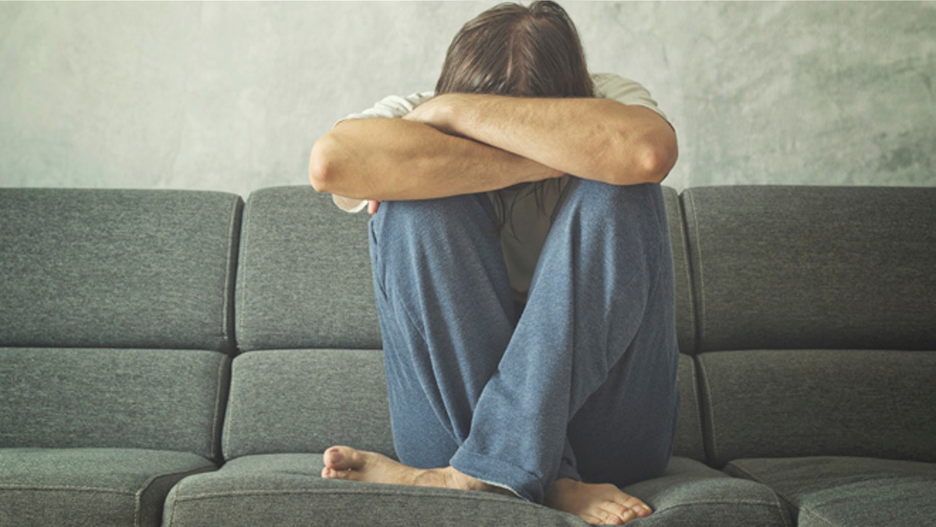Depressed and sad man on the couch in the room, covering face and crying in despair.