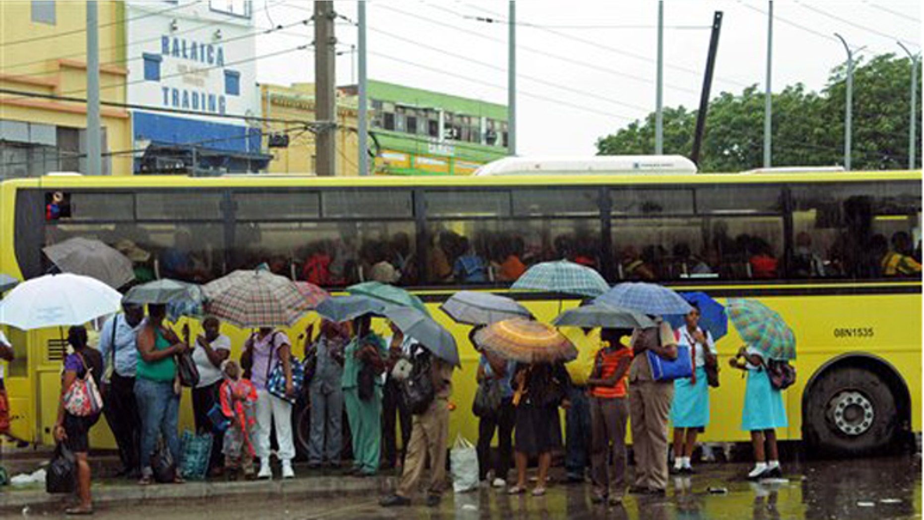 Commuters wait at a bus stop as rain brought by the outer bands of Tropical Storm Sandy falls in Kingston, Jamaica, Tuesday, Oct. 23, 2012. The U.S. National Hurricane Center in Miami said Sandy was expected to become a hurricane as it nears Jamaica on Wednesday. (AP Photo/Collin Reid)