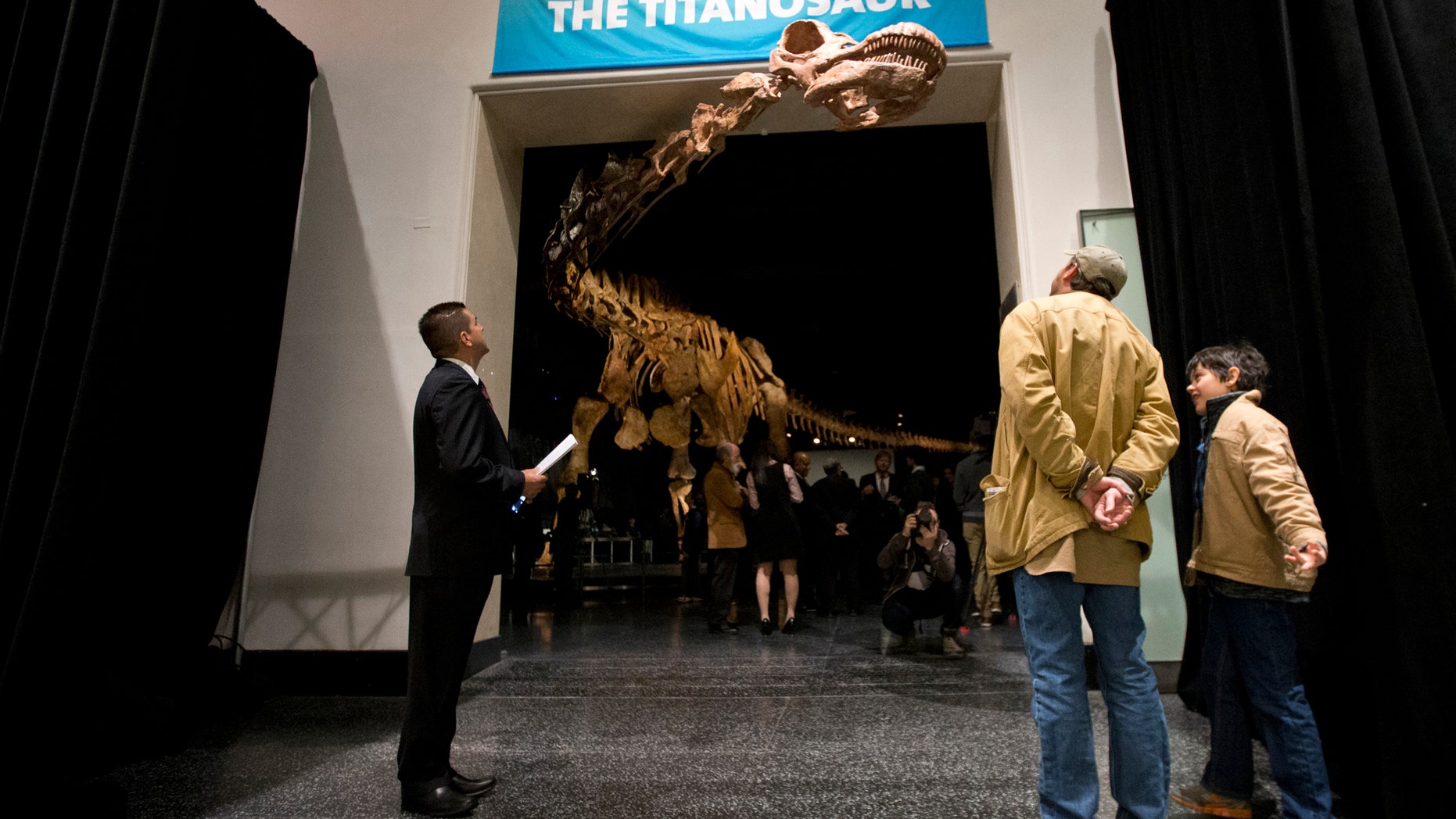 File-This Jan. 14, 2016, file photo shows visitors to the American Museum of Natural History examining a replica of a 122-foot-long dinosaur on display. A study proclaims a newly named species the heavyweight champion of all dinosaurs. (AP Photo/Mary Altaffer, File)