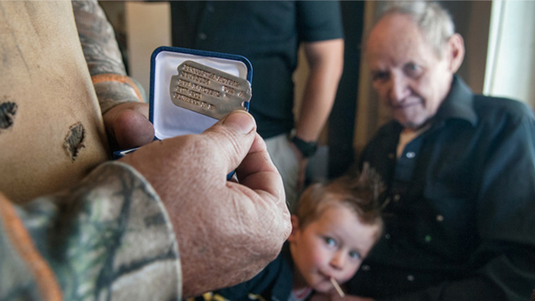 Joe Roy Roybal, right, with his great-grandson Albianjames Valdezhern, 2, watches as his brother Ivan Roybal pulls out the dog tag of their uncle Esquipula Roybal. (Eddie Moore/Albuquerque Journal)