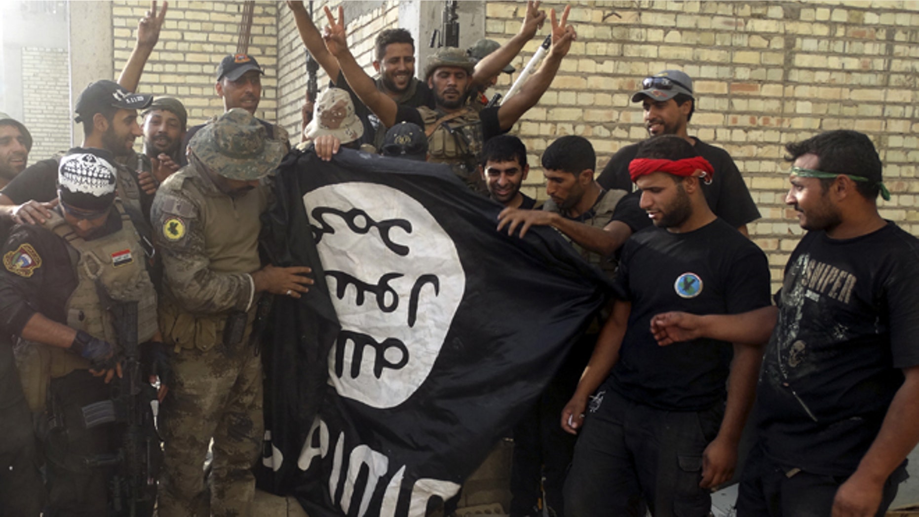 FILE 2015: Iraqi security forces stand with an Islamist State flag which they pulled down at the University of Anbar, in Anbar province.