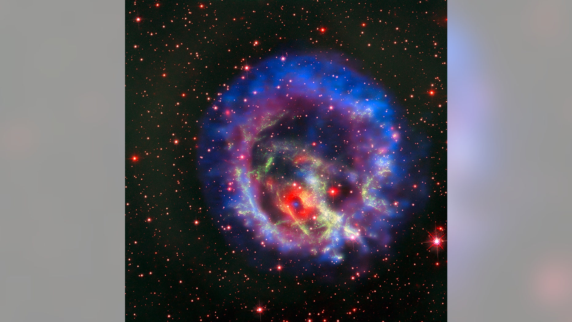 The new composite image of neutron star E0102, released on May 23, combines data from NASA's Chandra X-Ray Observatory (seen in blue and purple), the Multi Unit Spectroscopic Explorer instrument on the European Southern Observatory's Very Large Telescope in Chile (in bright red) and the Hubble Space Telescope (in dark red and green).