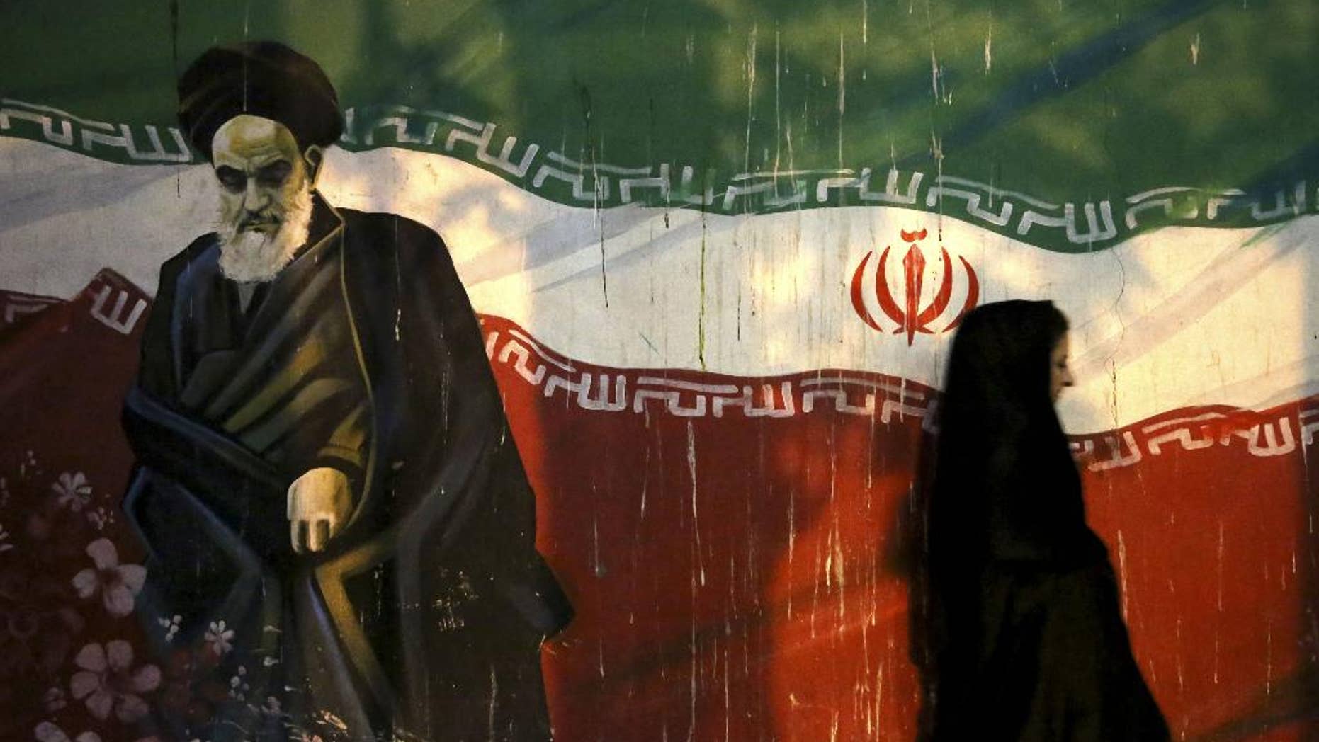 FILE - In this Nov. 2, 2013 file photo, a veiled Iranian woman walks past a mural depicting the late revolutionary founder Ayatollah Khomeini, and national Iranian flag, painted on the wall of the former U.S. Embassy, in Tehran, Iran. Siamak Namazi, an Iranian-American businessman who advocated better ties between Iran and the U.S. reportedly has been arrested and imprisoned in Tehran, becoming the fourth U.S. citizen known to be held there at a time when hard-liners are pushing back against the country's nuclear deal with world powers. Iranian officials could not be reached for comment Friday, Oct. 30, 2015, part of the Iranian weekend, and state media did not report on Namazi's reported detention. (AP Photo/Ebrahim Noroozi)