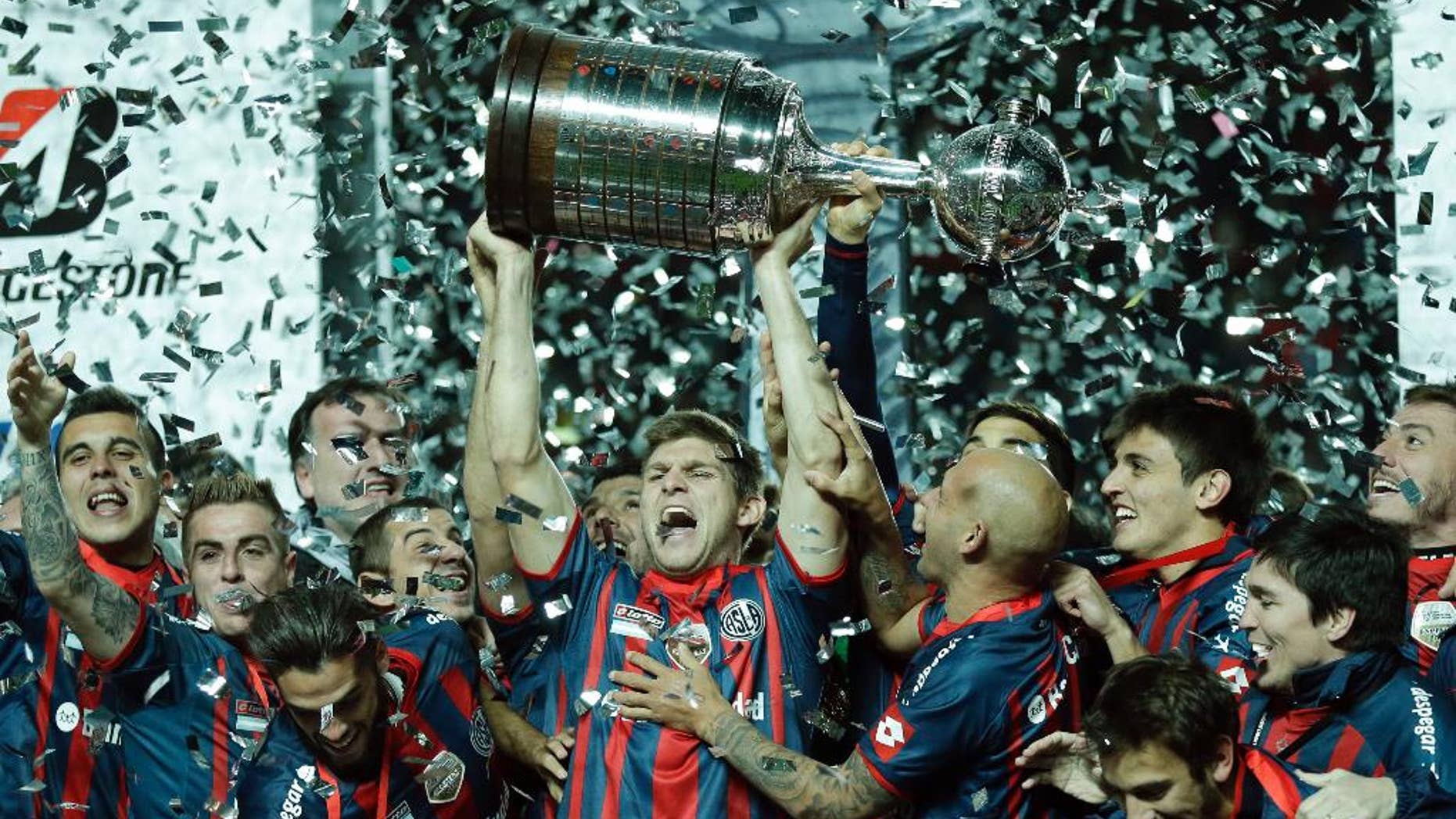 In this Aug. 13, 2014 photo, Walter Kannemann of Argentina's San Lorenzo, center, lifts the trophy after San Lorenzo won the 2014 Copa Libertadores championship against Paraguay's Nacional during the Copa Libertadores final soccer match in Buenos Aires, Argentina. The Argentine team, Pope Francis' favorite, defeated Nacional 2-1 on aggregate to win the title for the first time. (AP Photo/Victor R. Caivano)