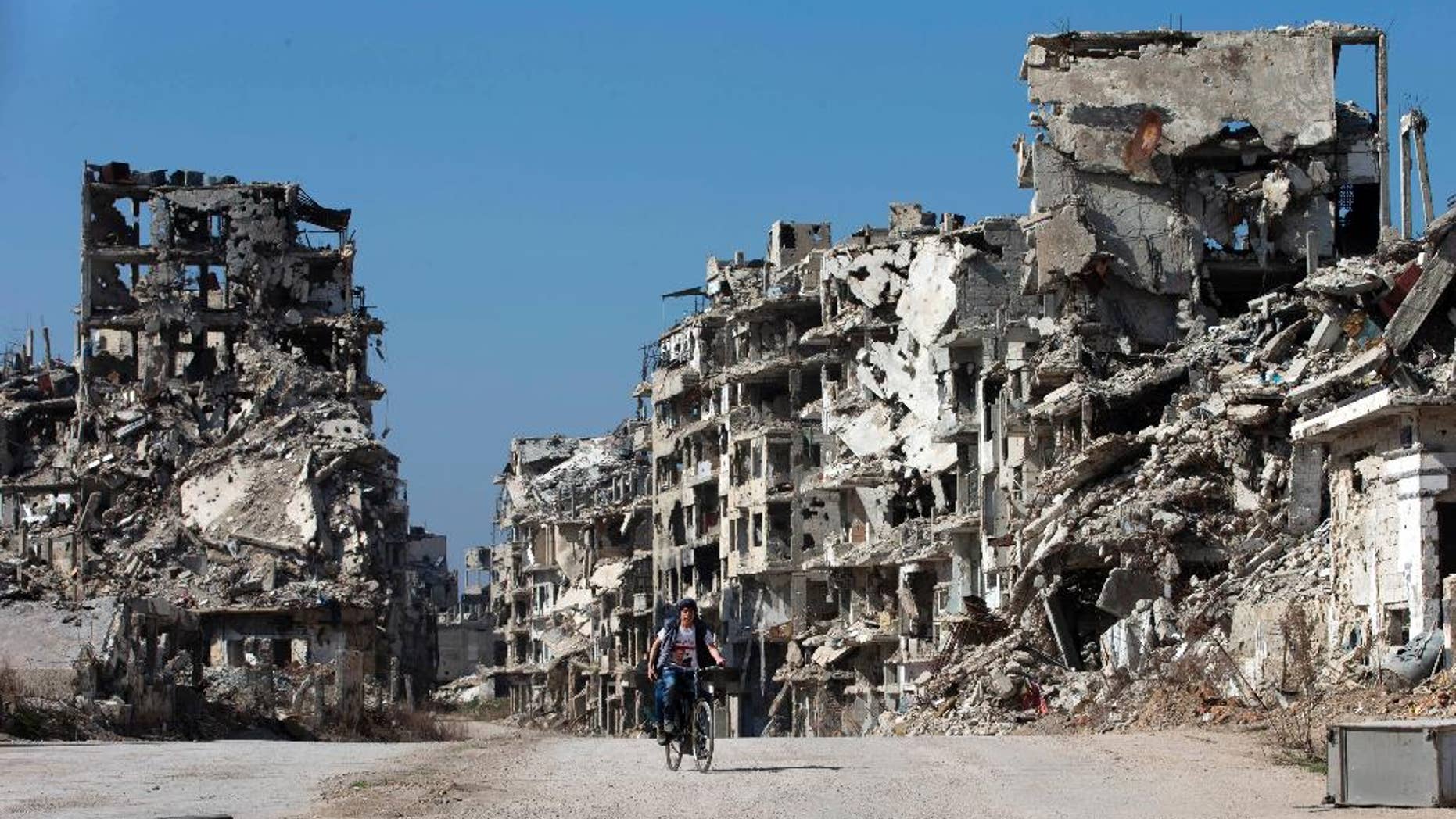 FILE -- In this February 26, 2016, file photo, a Syrian boy rides a bicycle through a devastated part of the old city of Homs, Syria. Syrian opposition fighters will be allowed to leave the last rebel-held neighborhood in the city of Homs under a Russia-backed deal signed on Monday, March 13, 2017, a Syrian official and an activist said.(AP Photo/Hassan Ammar, File)