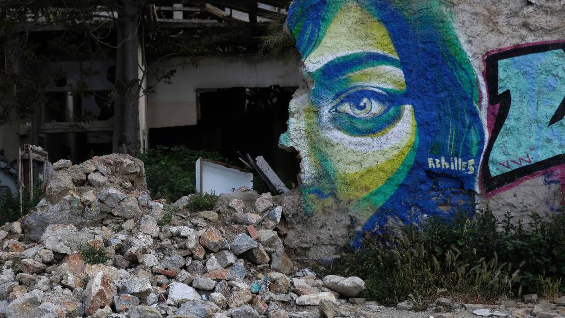 Graffiti by Greek street artist Achilles is seen on a wall of an abandoned house in central Athens, on Wednesday, April 22, 2015. Greece is running perilously short of cash amid an impasse in bailout talks with its international creditors. Eurozone finance ministers are to meet in Riga, Latvia on Friday but hopes of a deal on Greece there have diminished. (AP Photo/Petros Giannakouris)