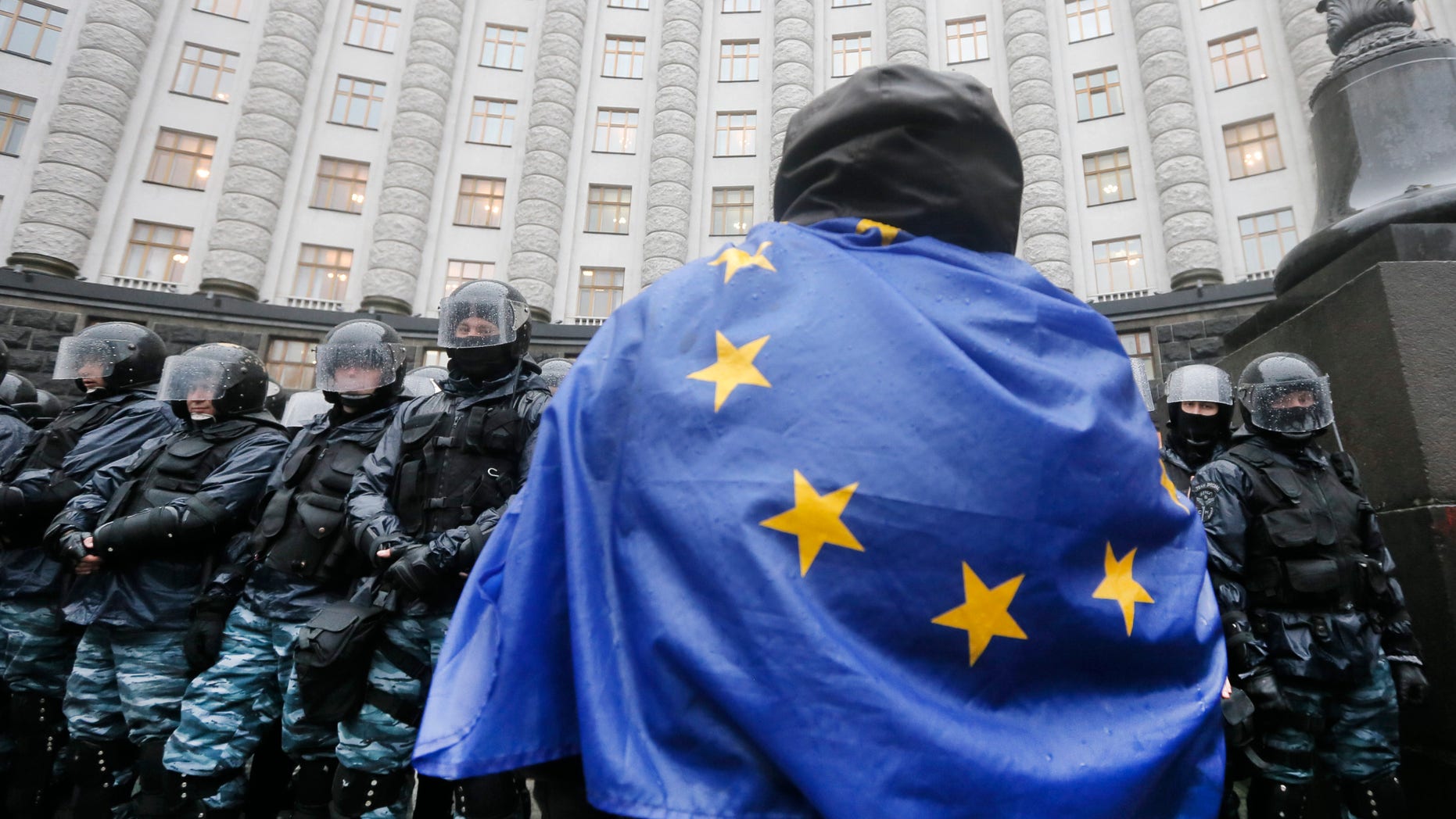 An opposition supporter draped in an EU flag, attends a protest in front of the Ukrainian Cabinet of Ministers in Kiev, Ukraine, Monday, Nov. 25, 2013. Hundreds of angry Ukrainians on Monday clashed with riot police outside the government building as protests continued in Kiev over the government’s abrupt decision to pause integration with the West and tilt toward Moscow. The scuffle Monday morning follows a large protest in the heart of Kiev Sunday, the biggest since the 2004 Orange Revolution that brought a pro-Western government to power. Tens of thousands of people turned up to protest President Viktor Yanukovych’s decision to snub a potentially historic deal with the EU and focus on ties with Moscow, after immense pressure from Russia. (AP Photo/Efrem Lukatsky)