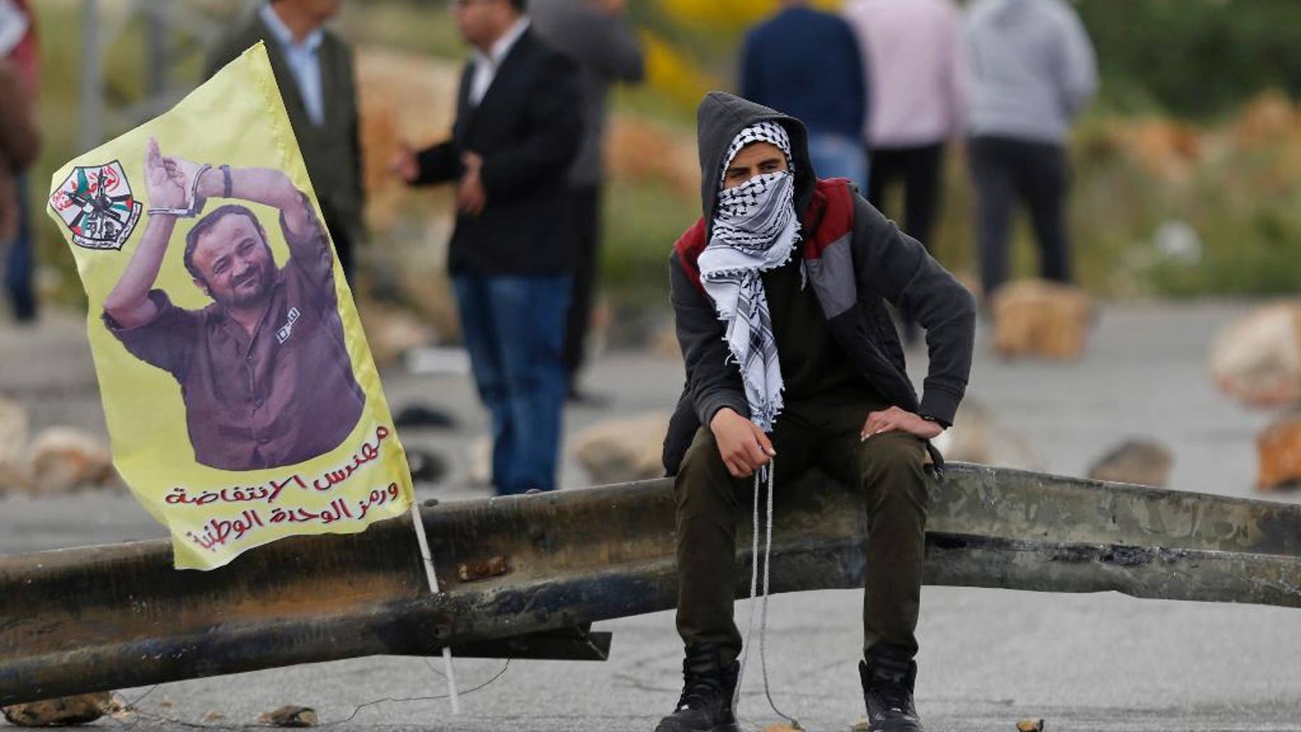 FILE -- In this April 23, 2017 file photo, a Palestinian protester holds a sling shot as he sits near a banner with a picture of jailed leader Marwan Barghouti that reads, "The architect of the uprising," following a protest supporting prisoners in Israeli jails, in the West Bank city of Ramallah. An Israeli official said Monday, May 1, 2017, that the number of Palestinians prisoners participating in one of the largest hunger strike in years dropped to 870, from 1,300 a week earlier. Support for the hunger strikers who seek better conditions has gained momentum with West Bank marches and a social media campaign and has boosted the Palestinian leadership credentials of its imprisoned organizer, Barghouti. (AP Photo/Majdi Mohammed, File)