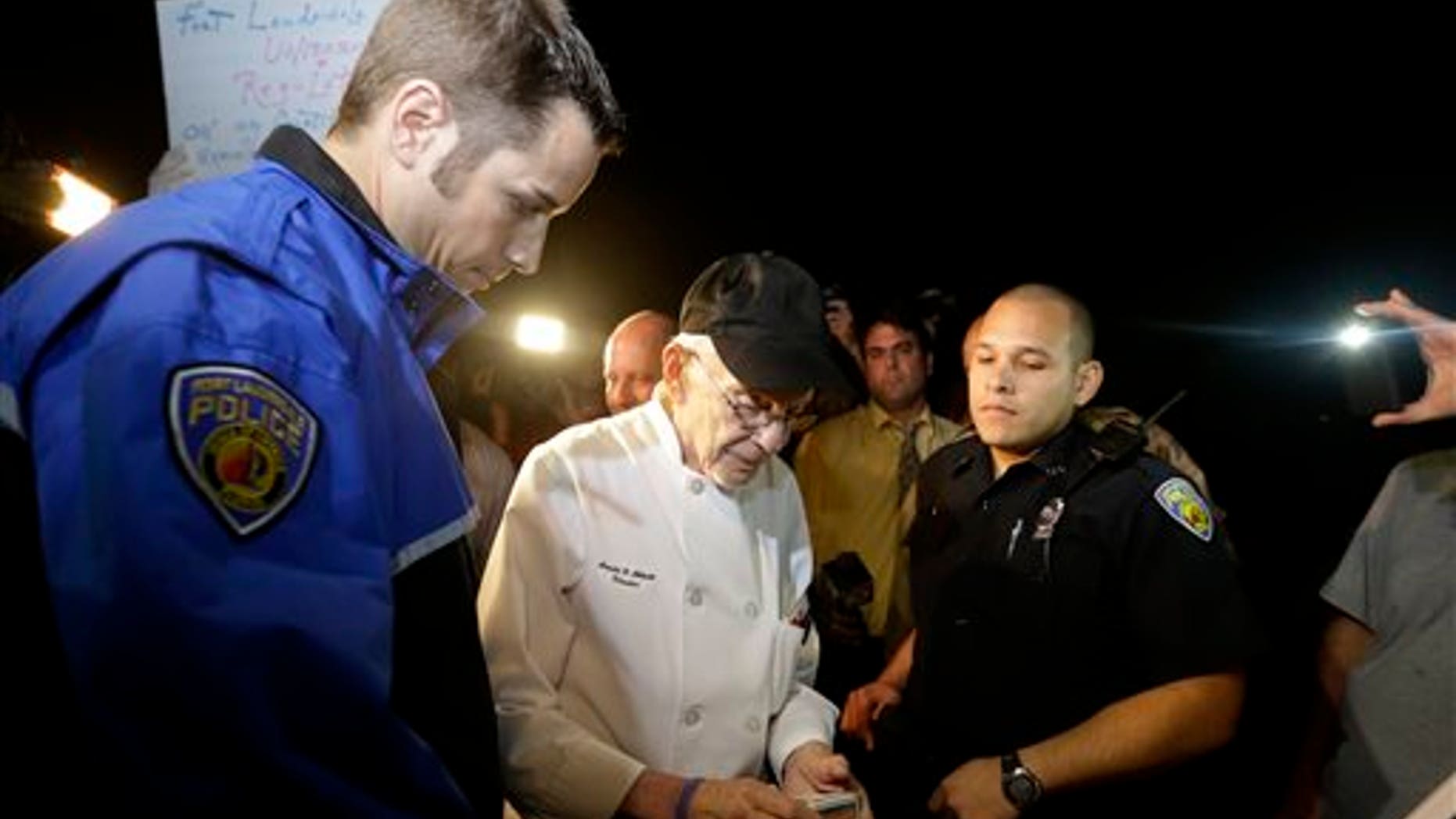 Homeless advocate Arnold Abbott, 90, of the nonprofit group Love Thy Neighbor Inc., center, gets his drivers license to hand to a Fort Lauderdale police officer, Wednesday, Nov. 5, 2014, in Fort Lauderdale, Fla. Abbott and a group of volunteers were feeding the homeless in a public parking lot next to the beach when he was issued a summons to appear in court for violating an ordinance that limits where charitable groups can feed the homeless on public property. Abbott w also recently arrested along with two pastors for feeding the homeless in a Fort Lauderdale park. (AP Photo/Lynne Sladky)