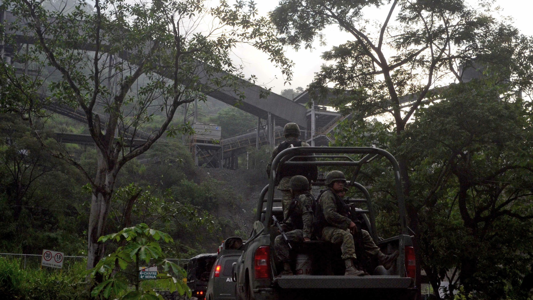 In this Aug. 14, 2013 photo, Mexican army soldiers enter the iron ore mine in the town of Aquila, Mexico. A resident of Aquila, said that since 2012, the Knights Templar cartel demanded residents hand over part of the royalty payments from the local iron ore mine operated by Ternium, a Luxembourg-based consortium. Mexican drug cartels long ago moved into oil theft, pirated goods, extortion and kidnapping, but it still came as a shock this month when federal officials revealed the gangs have broadened the scope and sophistication of their economic empires by entering the country’s lucrative mining industry, exporting iron ore to Chinese and other foreign mills. (AP Photo/Agencia Esquema)