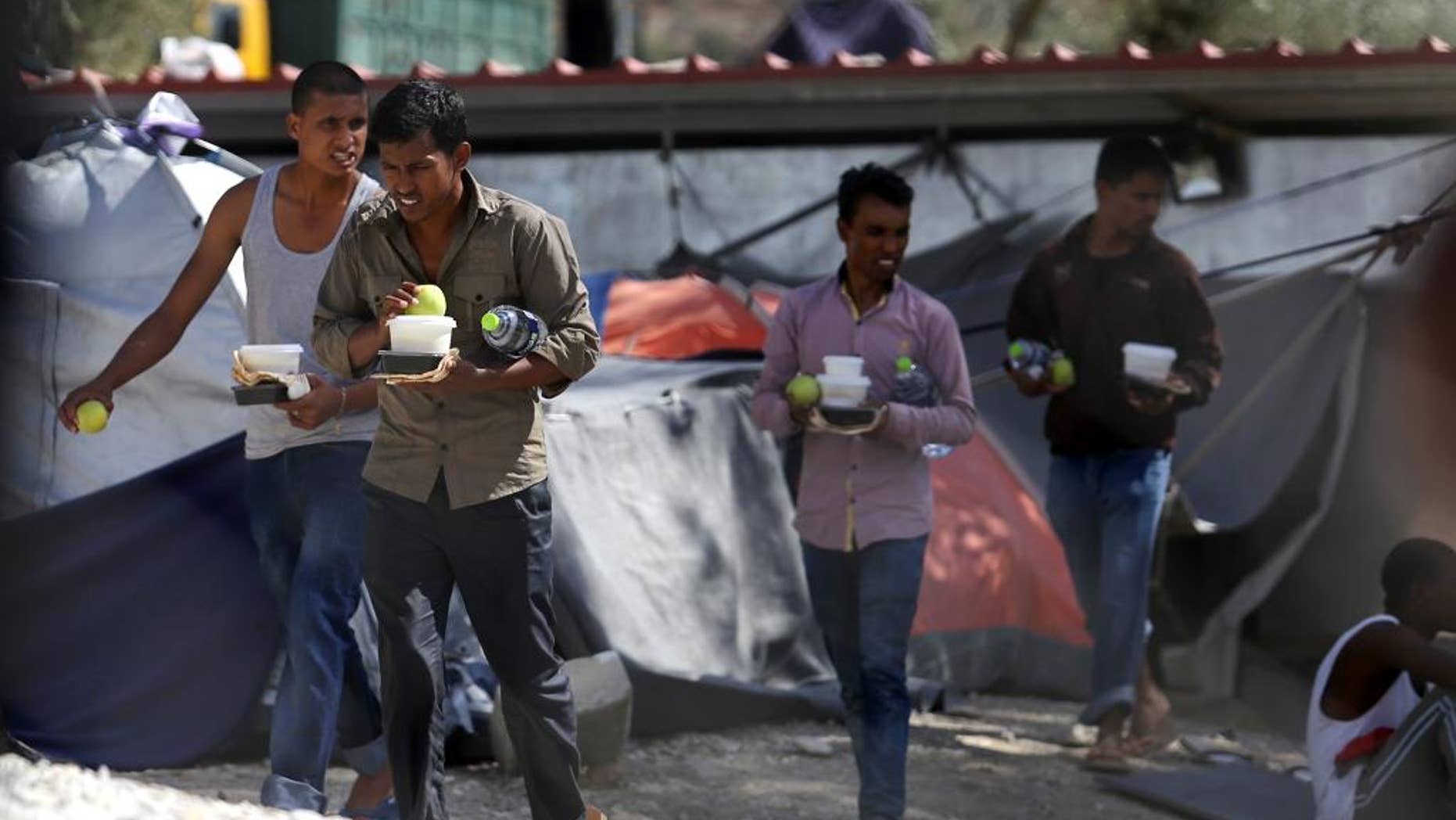Migrants carry food at the Moria refugee camp on the northeastern Greek island of Lesbos, on Tuesday, Sept. 20, 2016, after a fire gutted the camp following protests at the camp. Authorities of the island of Lesbos are calling for the immediate evacuation of thousands of refugees to the Greek mainland, following the fire and nine migrants suspected of starting the blaze have been arrested, authorities said Tuesday. (Dimitris Tosidis/InTime News via AP)